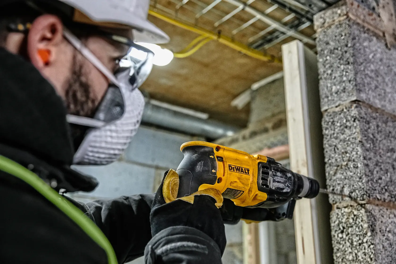 Um trabalhador com equipamento de segurança está usando um martelete amarelo DEWALT (modelo D25133K) para perfurar uma parede de concreto em um canteiro de obras.