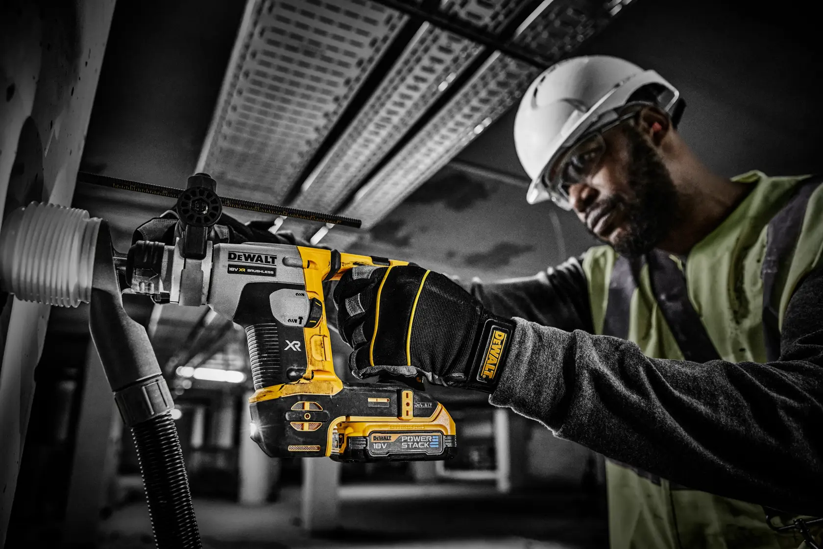 Trabalhador perfura parede com ferramenta DEWALT PowerStack 18V, usando luvas e capacete.