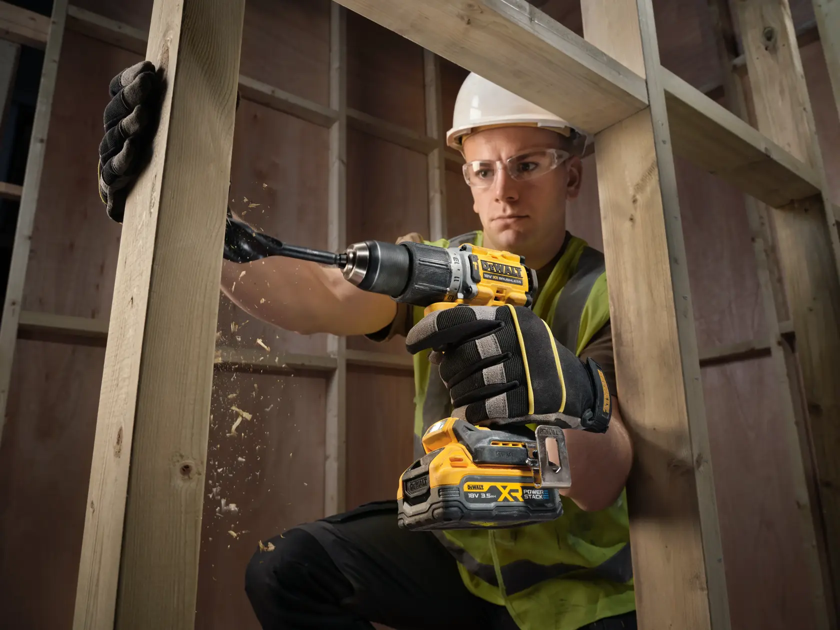 Trabalhador perfura viga de madeira com furadeira DEWALT sem fio, usando luvas e equipamento.