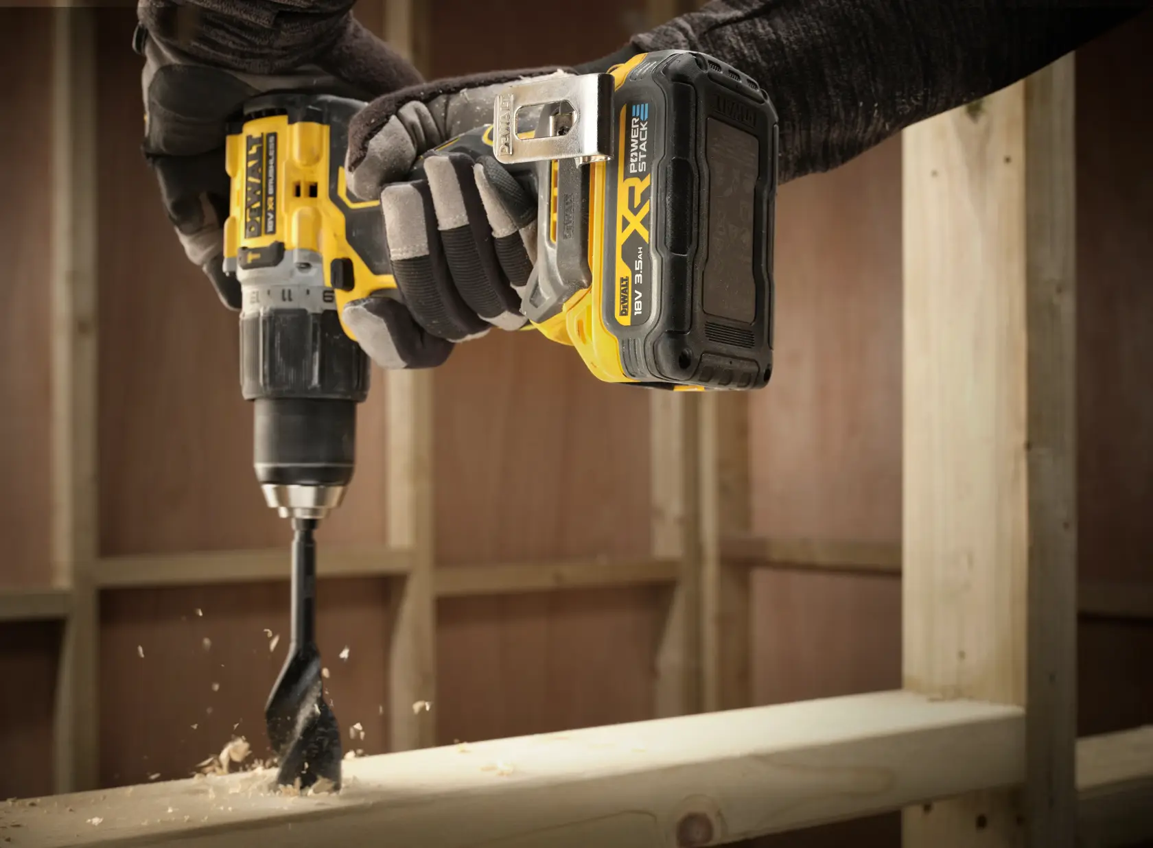 Close-up de uma furadeira DEWALT com bateria DCBP318, furando madeira em um canteiro de obras.
