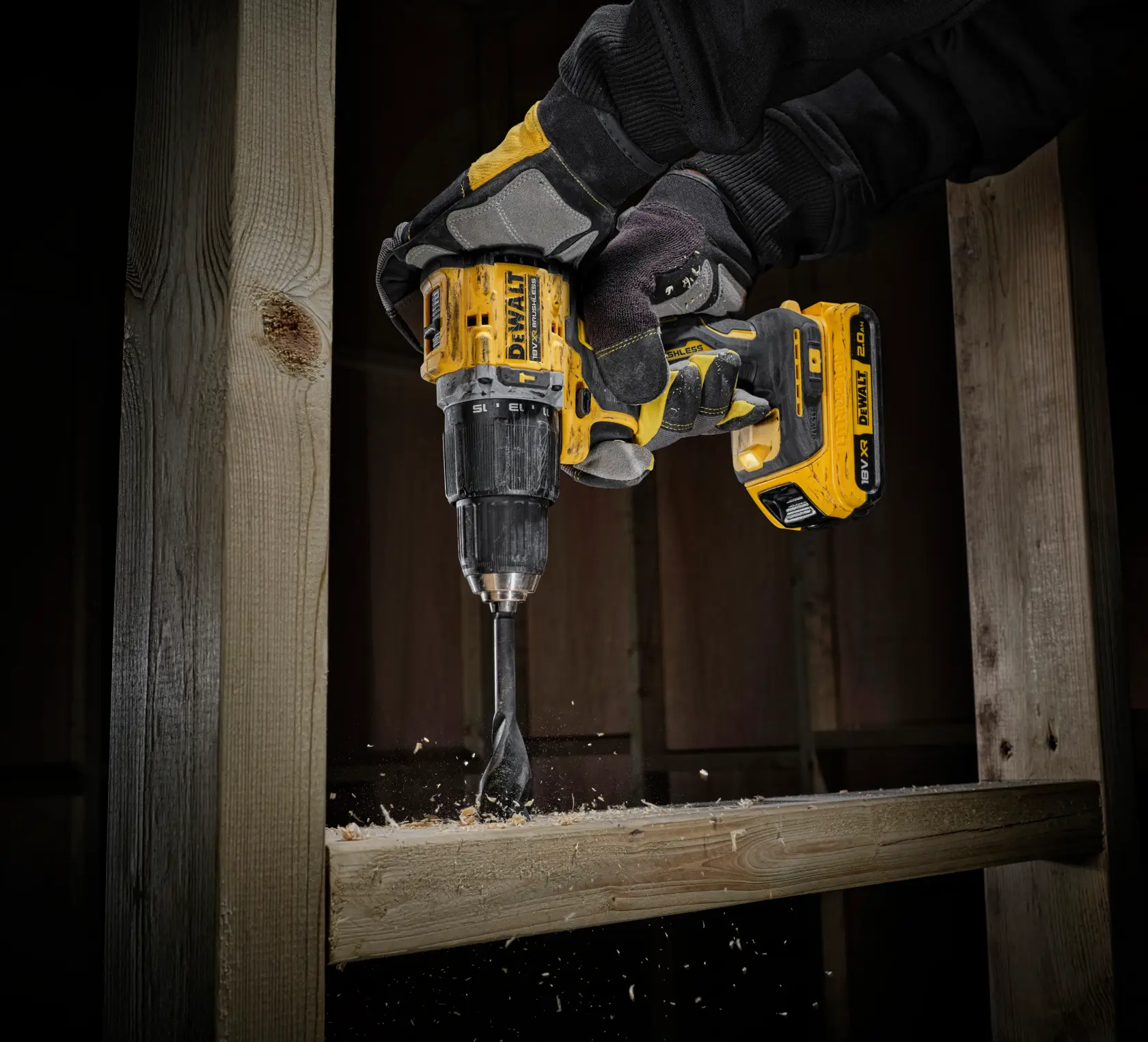 Mano enguantada taladra madera con DEWALT inalámbrico, virutas de madera volando.