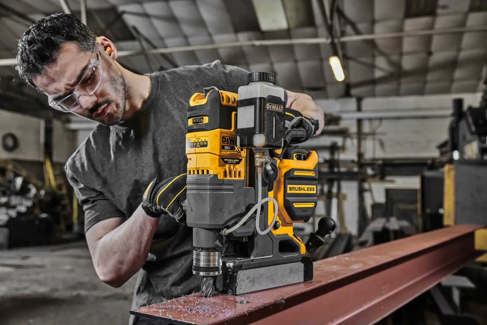 Furadeira brushless DEWALT DCD1623N usada em viga de aço na oficina por pessoa com rosto oculto.