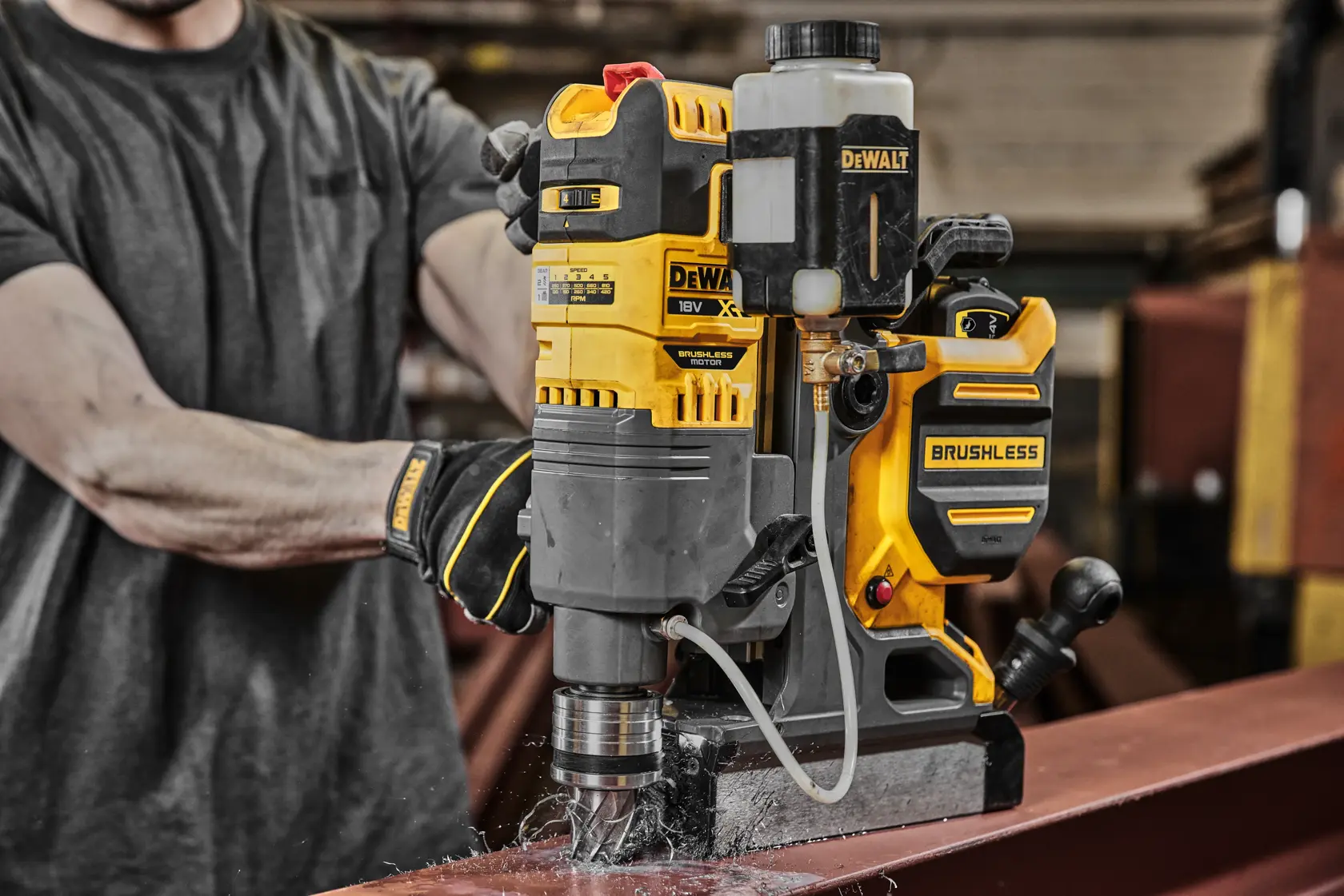 Furadeira magnética brushless DEWALT perfura viga de aço em ambiente de oficina industrial.