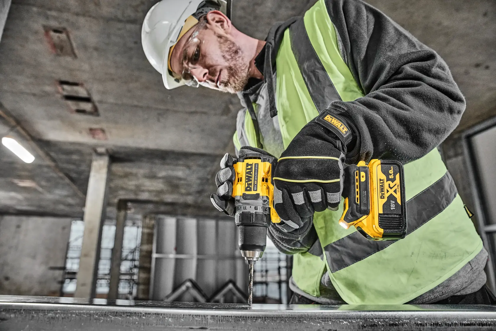 Una persona con equipo de seguridad, incluidos guantes, casco y chaleco reflectante, utiliza un taladro inalámbrico DEWALT DCD800P2T para trabajar sobre una superficie metálica en un entorno industrial.