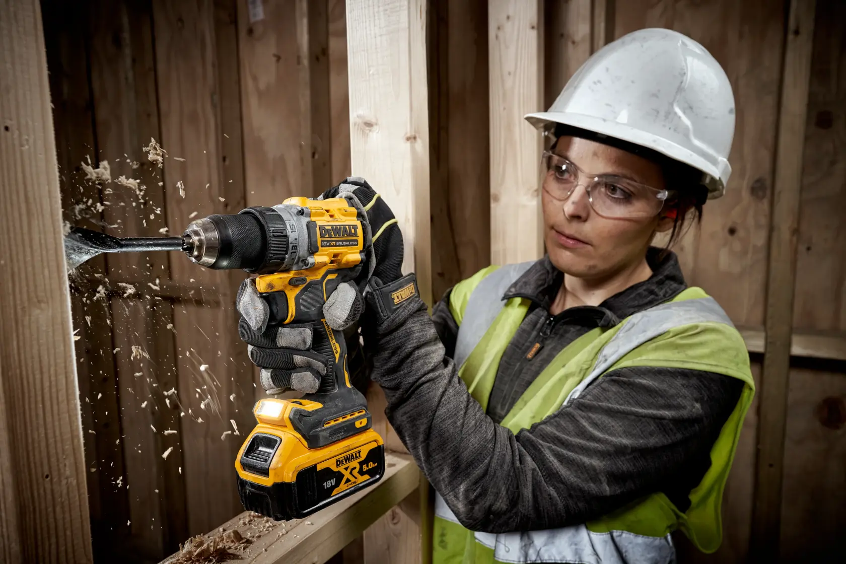 Persona perfora madera con DEWALT DCD800P2T, con casco y guantes en obra de construcción.