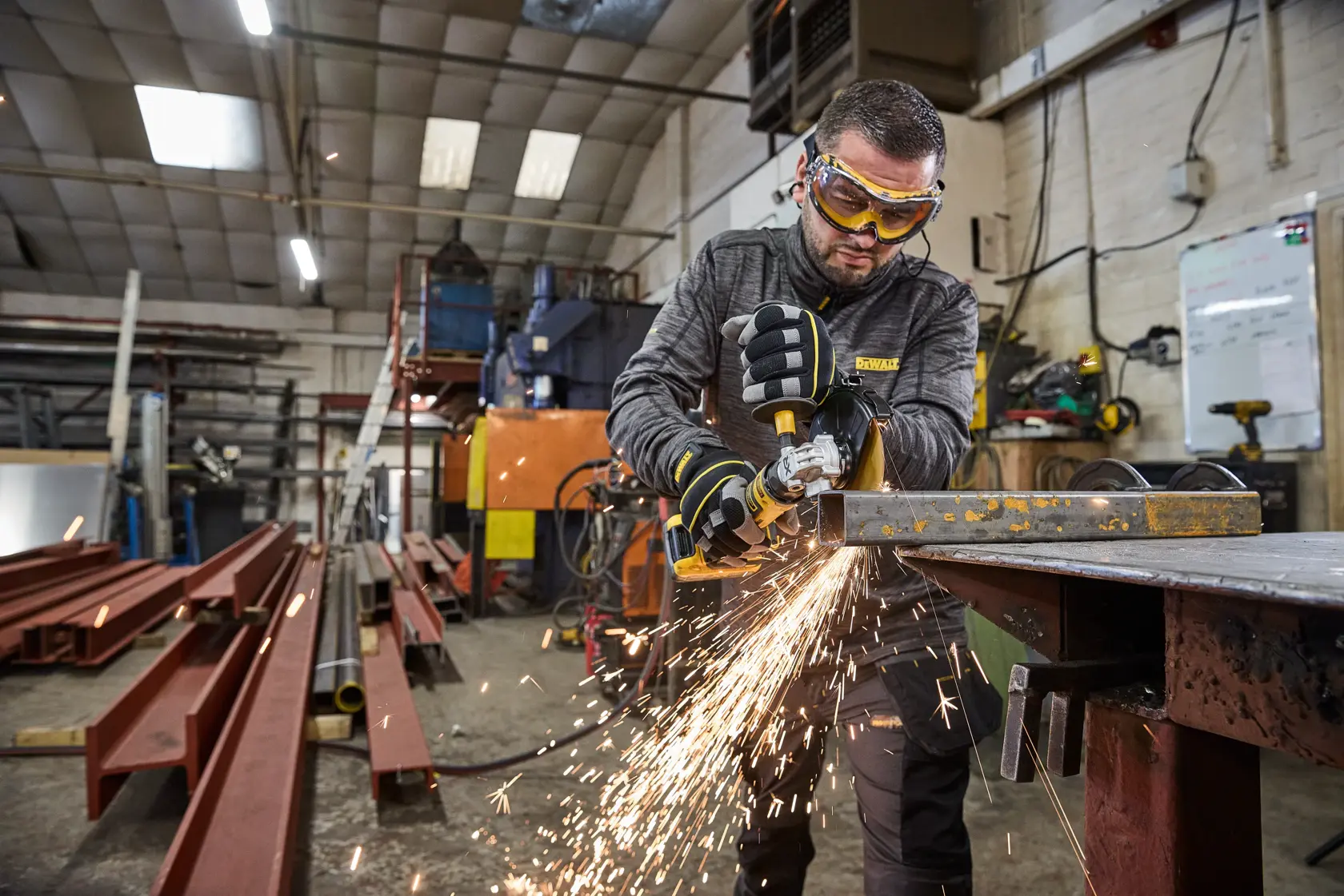 Pessoa usa esmerilhadeira DEWALT em metal na oficina, gerando faíscas. Equipamento industrial ao redor.