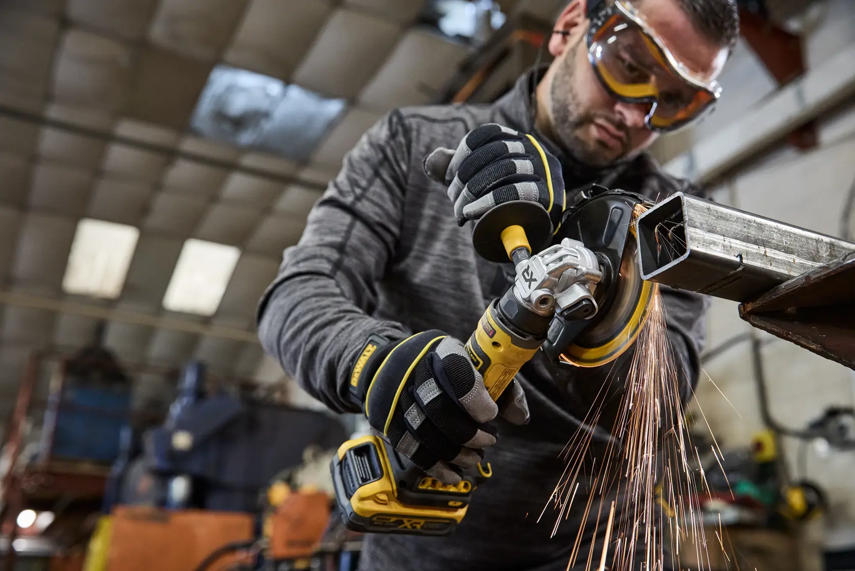 Pessoa usa esmerilhadeira sem fio DEWALT em metal, com faíscas, em oficina industrial.
