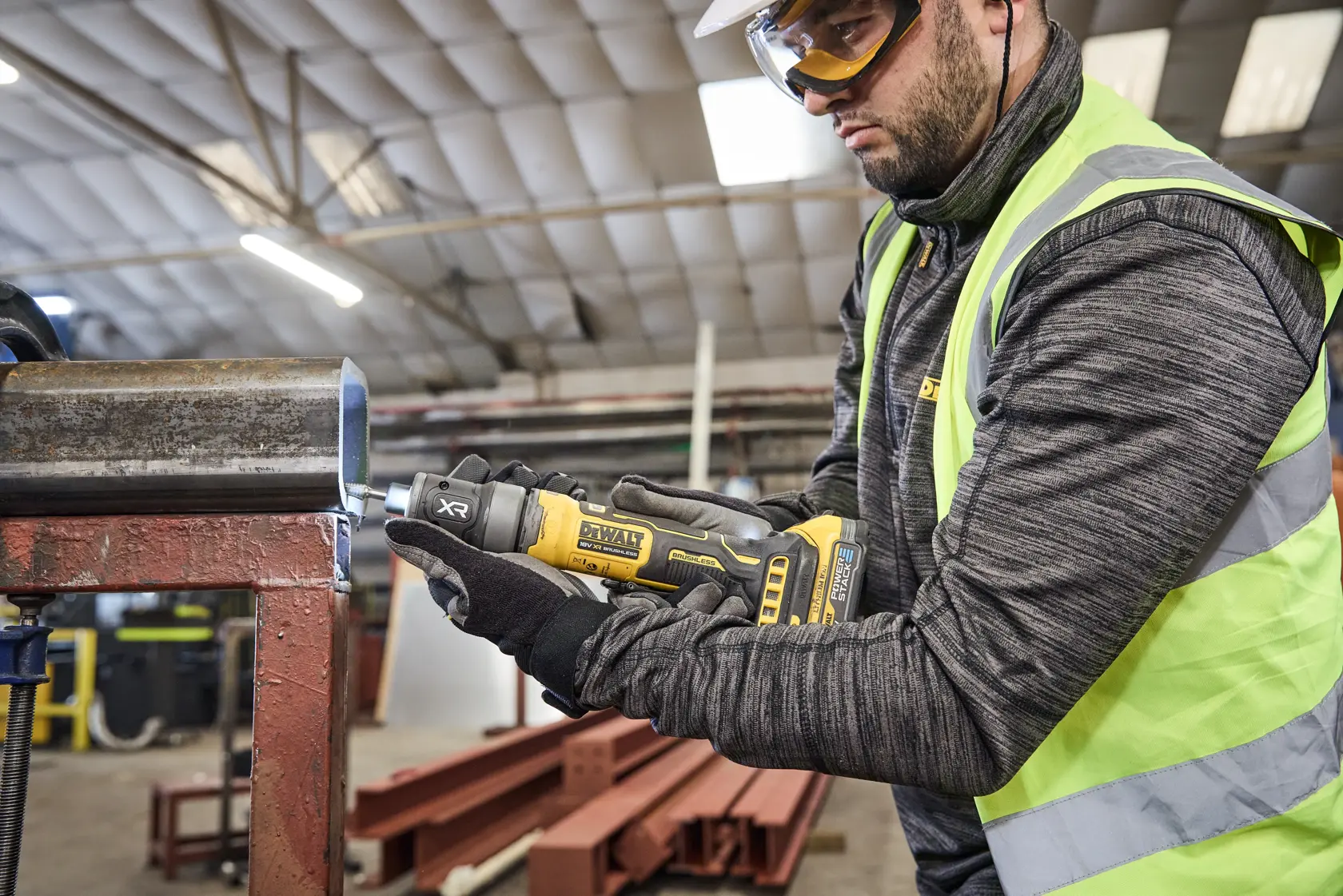 Trabalhador usa DEWALT DCG420N-XJ e DCG420N em tubo metálico em ambiente industrial.