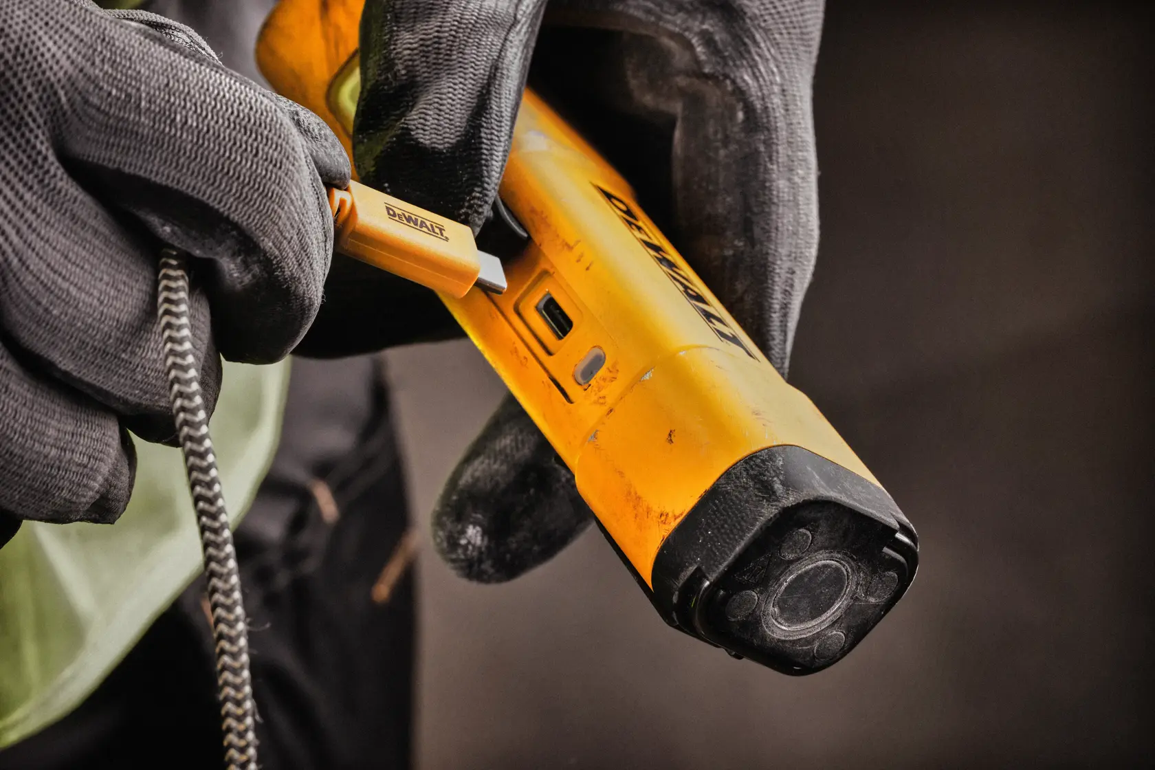 Primer plano de una mano enguantada conectando un cable USB a una lámpara de trabajo portátil amarilla DEWALT DCL183.