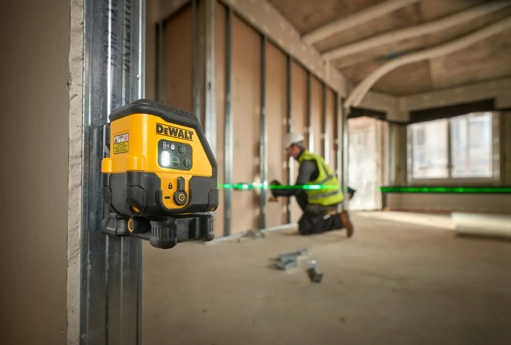 Nivel láser DEWALT proyecta línea verde en obra. Trabajador instala paneles de pared.