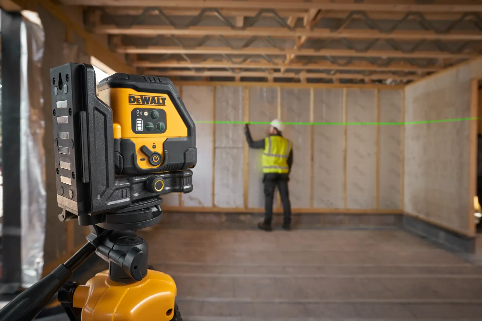 Nivel láser DEWALT sobre trípode proyectando línea verde en obra con trabajador marcando la pared.