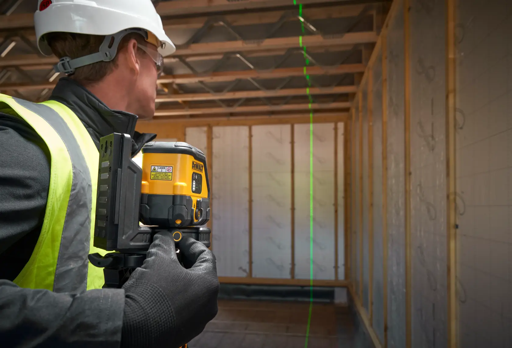 Trabajador usa nivel láser DEWALT proyectando línea verde vertical en edificio sin terminar.