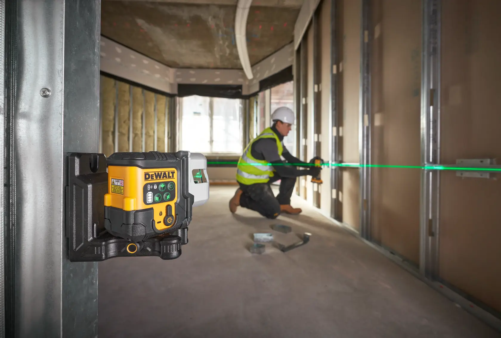 Nível a laser DEWALT projeta linha verde, usado por trabalhador para alinhar paredes na construção.