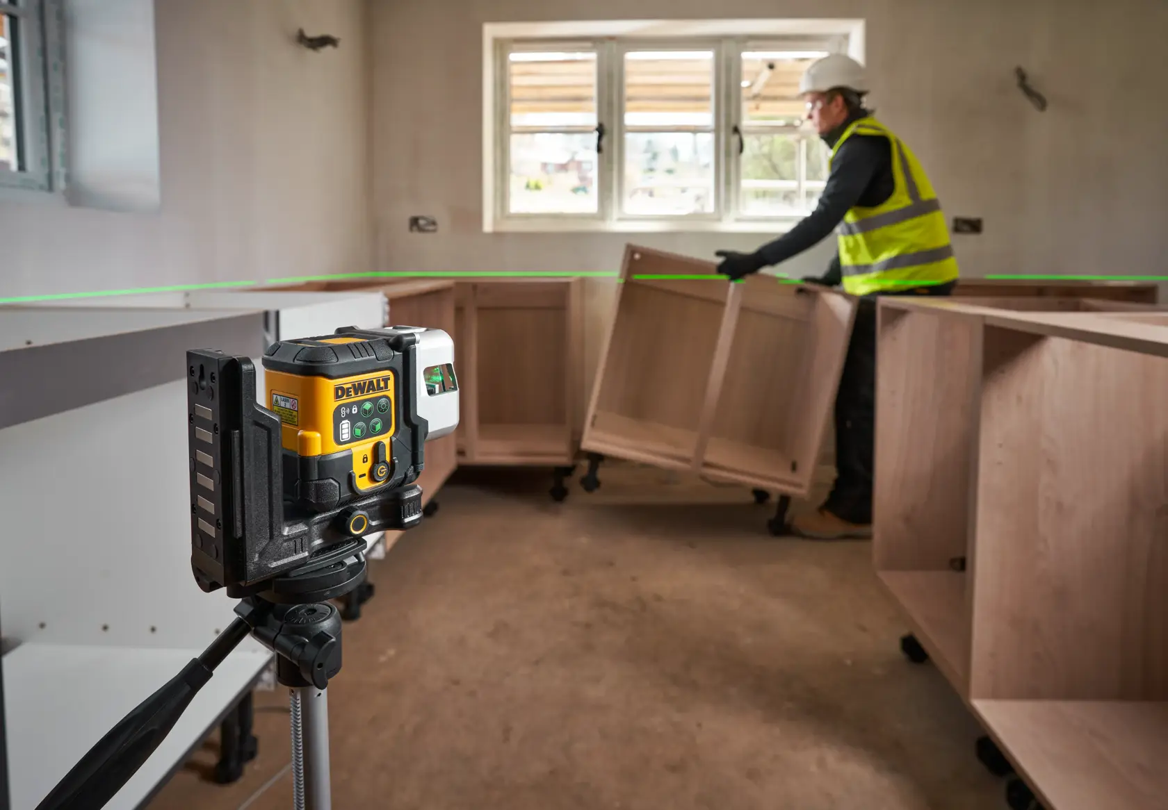 Nível a laser DEWALT em tripé projeta linha verde em sala com instalação de armários.