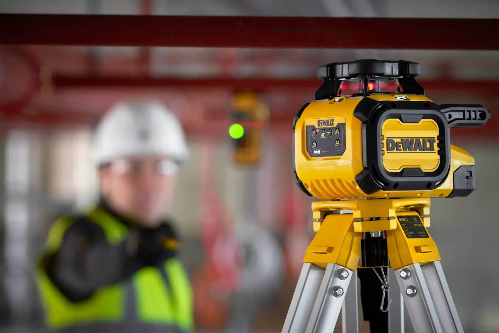 Laser DEWALT no tripé, SKUs DCLE15211R e DCLE15211R-QW, construção, trabalhador desfocado.