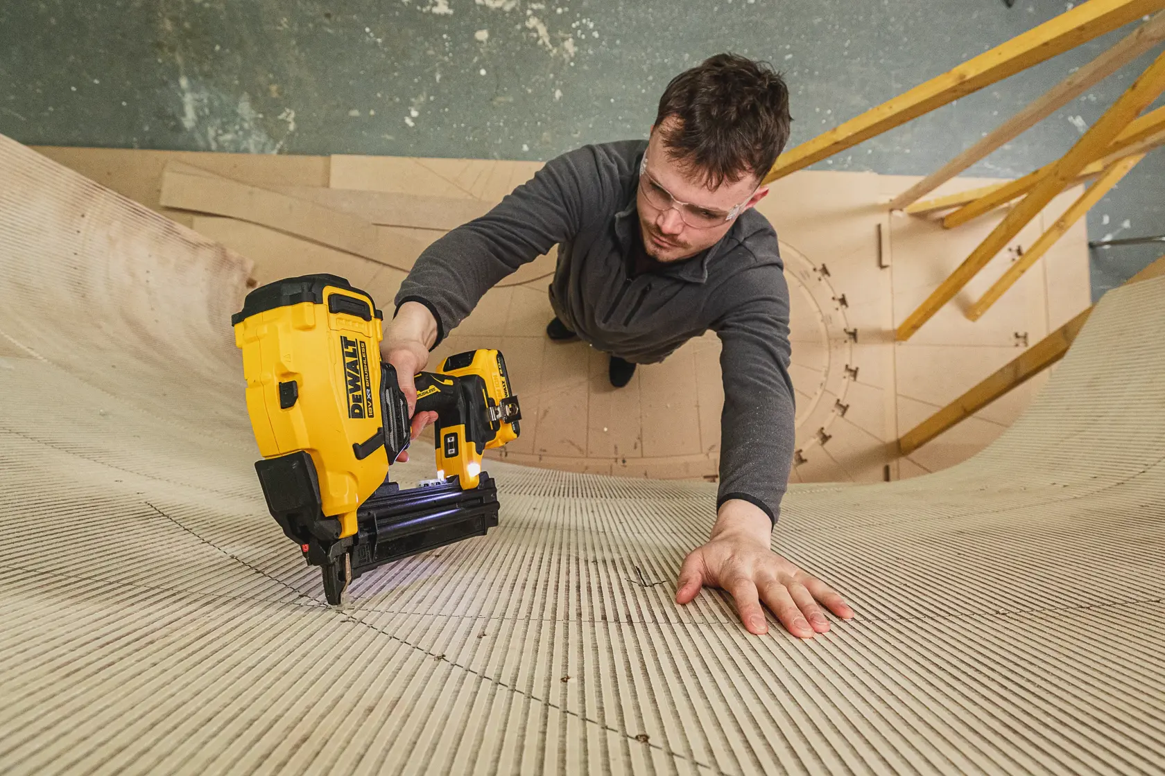 Pessoa utiliza uma pregadora DEWALT DCN210SN-XJ para fixar painéis de madeira curvos em oficina.