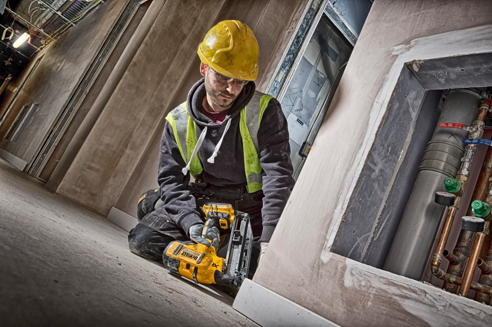 Trabajador usa clavadora DEWALT DCN660D2 en zócalo, arrodillado, con casco y chaleco de seguridad.