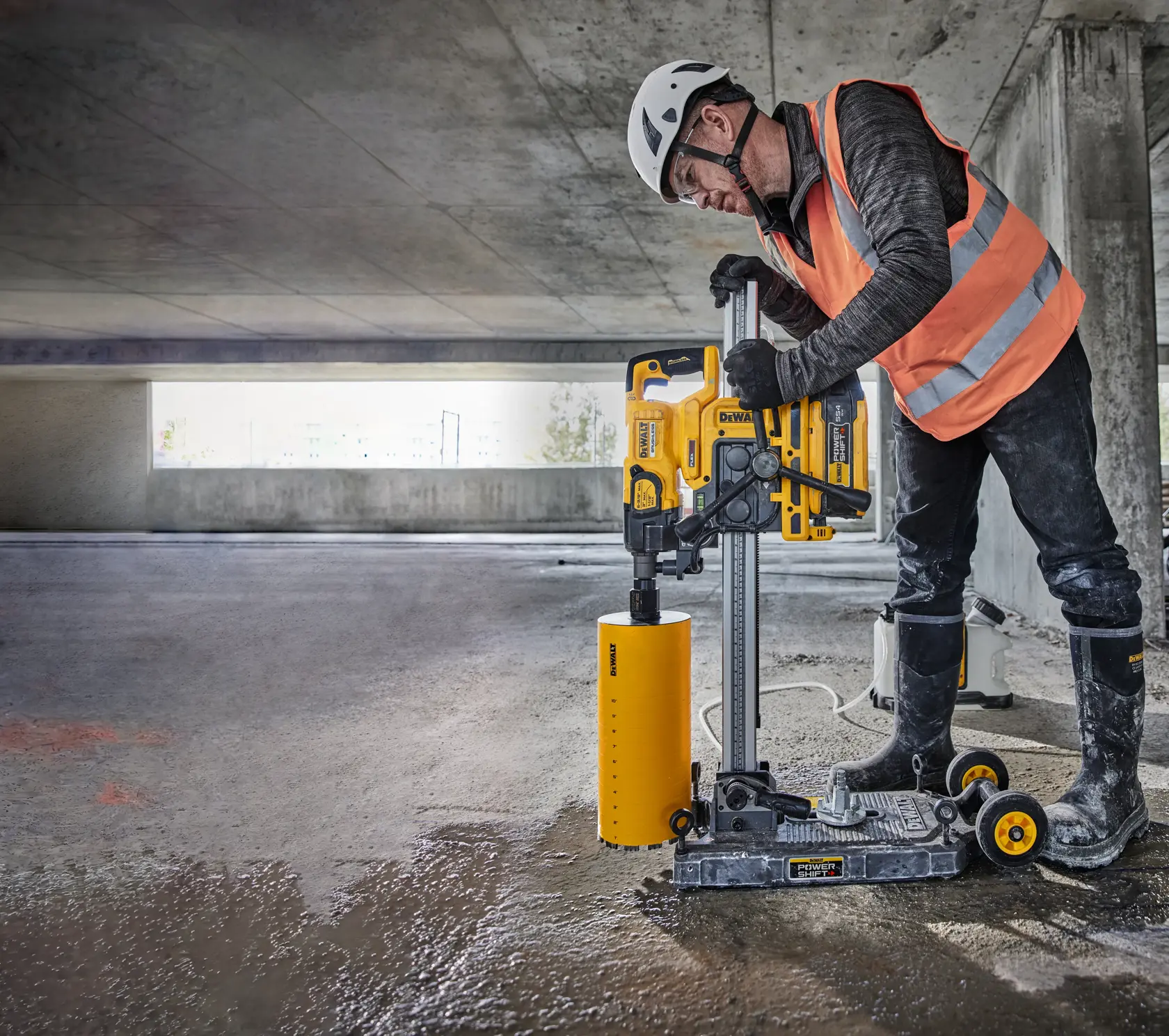 Vista aproximada de uma furadeira de núcleo DEWALT modelo DCPS151 montada em um trilho vertical, destacando seus controles de usuário espelhados e o mecanismo de travamento. O texto sobreposto diz « CONTROLES DE USUÁRIO ESPELHADOS - TRAVE A FURADEIRA DE NÚCLEO NO LUGAR ».
