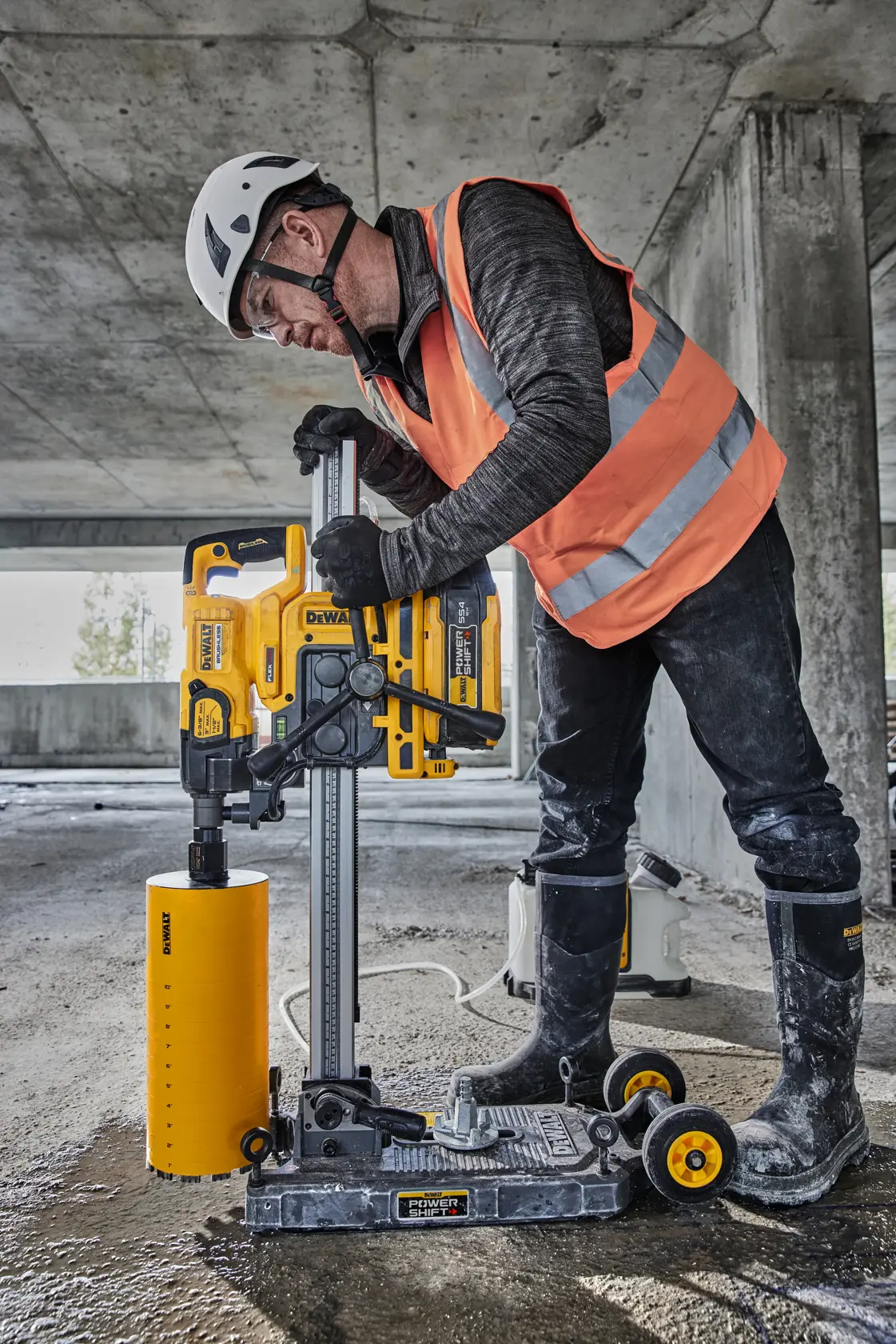 Trabalhador da construção usando capacete de segurança e colete laranja de alta visibilidade segurando uma ferramenta DEWALT em frente a um caminhão de obra em um canteiro de obras. O rosto do trabalhador está desfocado para preservar a privacidade.