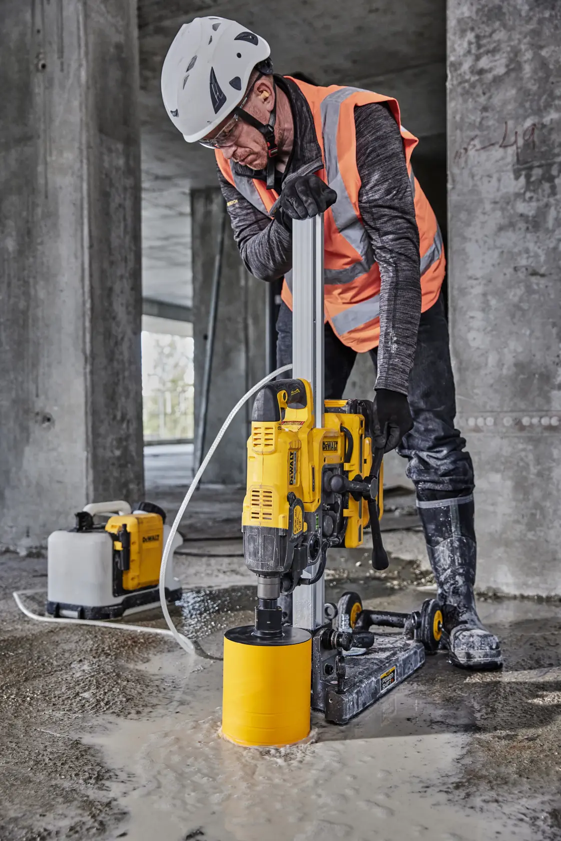 Um trabalhador usando equipamentos de segurança, incluindo capacete e colete de alta visibilidade, utiliza uma ferramenta sem fio DEWALT para cortar ou aparar equipamentos em um canteiro de obras. Estojos e ferramentas DEWALT estão visíveis na bancada.