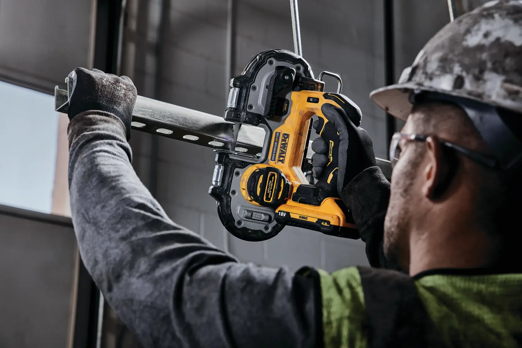 Persona usando sierra de cinta inalámbrica DEWALT para cortar tubo de metal, con guantes y casco.