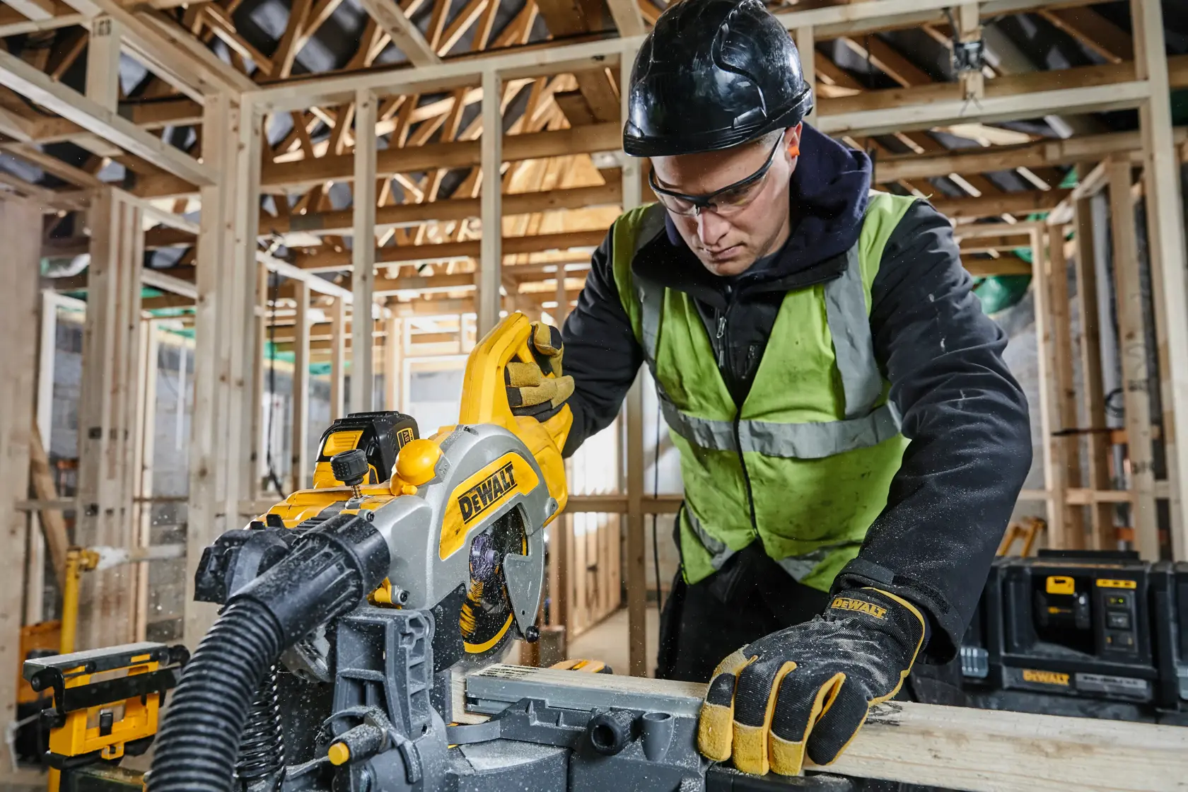Trabajador corta madera con DEWALT DCS777T2 en obra, usando equipo de protección y guantes.