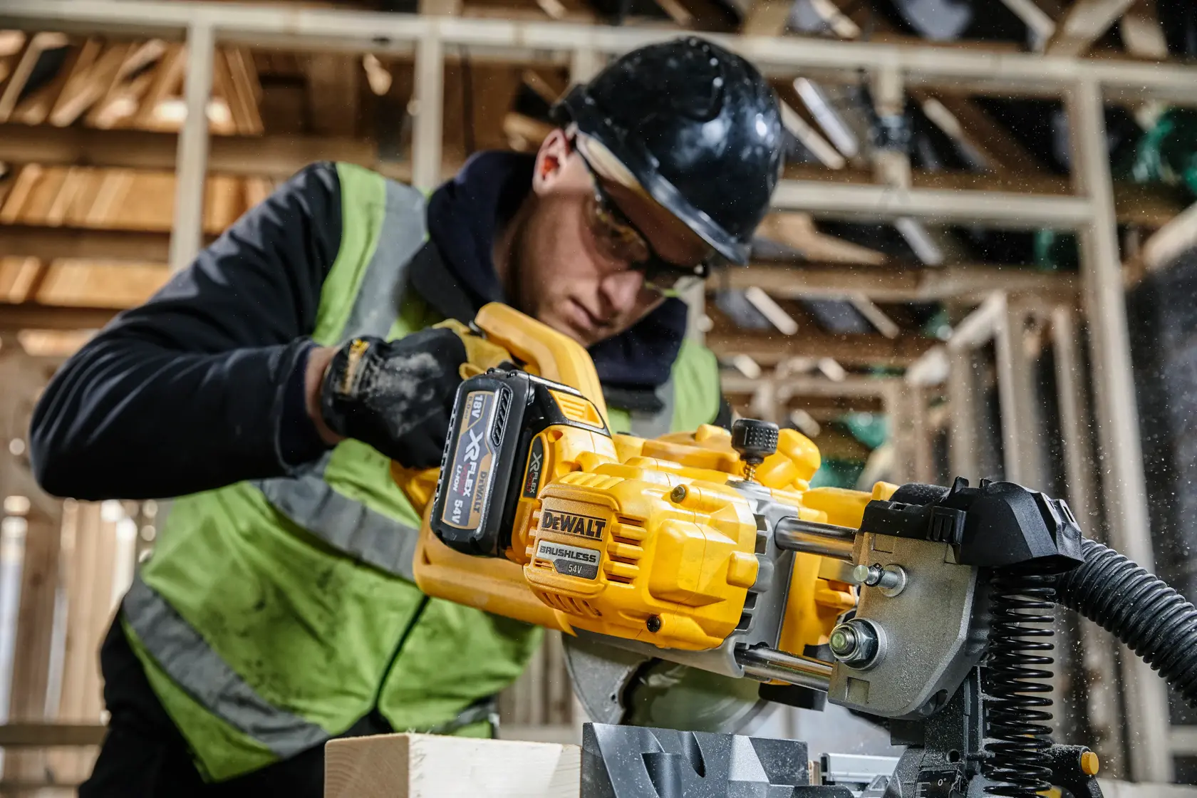 Trabajador usando sierra inalámbrica DEWALT DCS777T2 en obra de madera, con chaleco y casco.