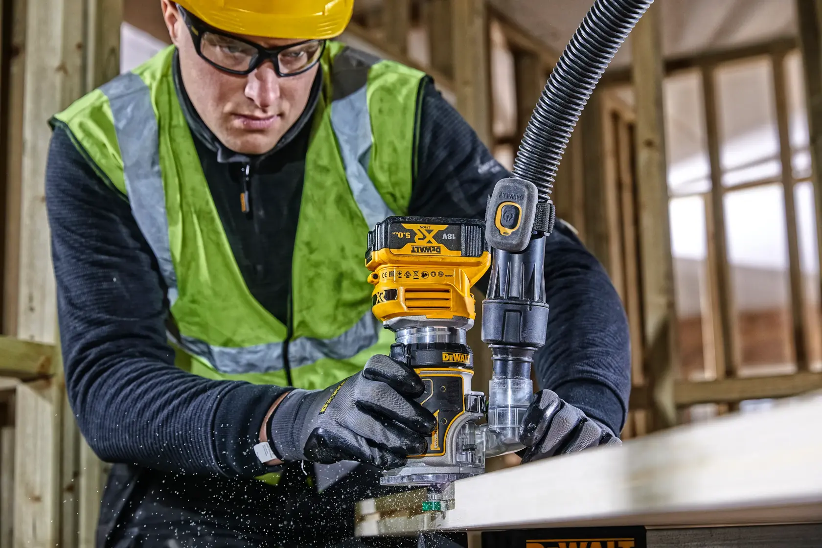 Persona usando una fresadora DEWALT DCW604 en madera, con equipo de seguridad en un sitio de construcción.