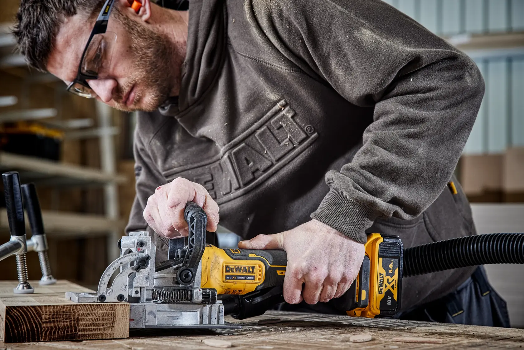Persona usando una DEWALT DCW682N inalámbrica en madera en taller, conectada a una manguera de extracción de polvo.