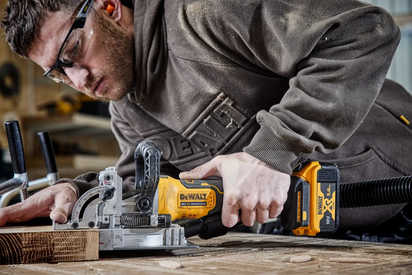 Persona utiliza la fresadora inalámbrica DEWALT DCW682N en madera, entorno de taller.