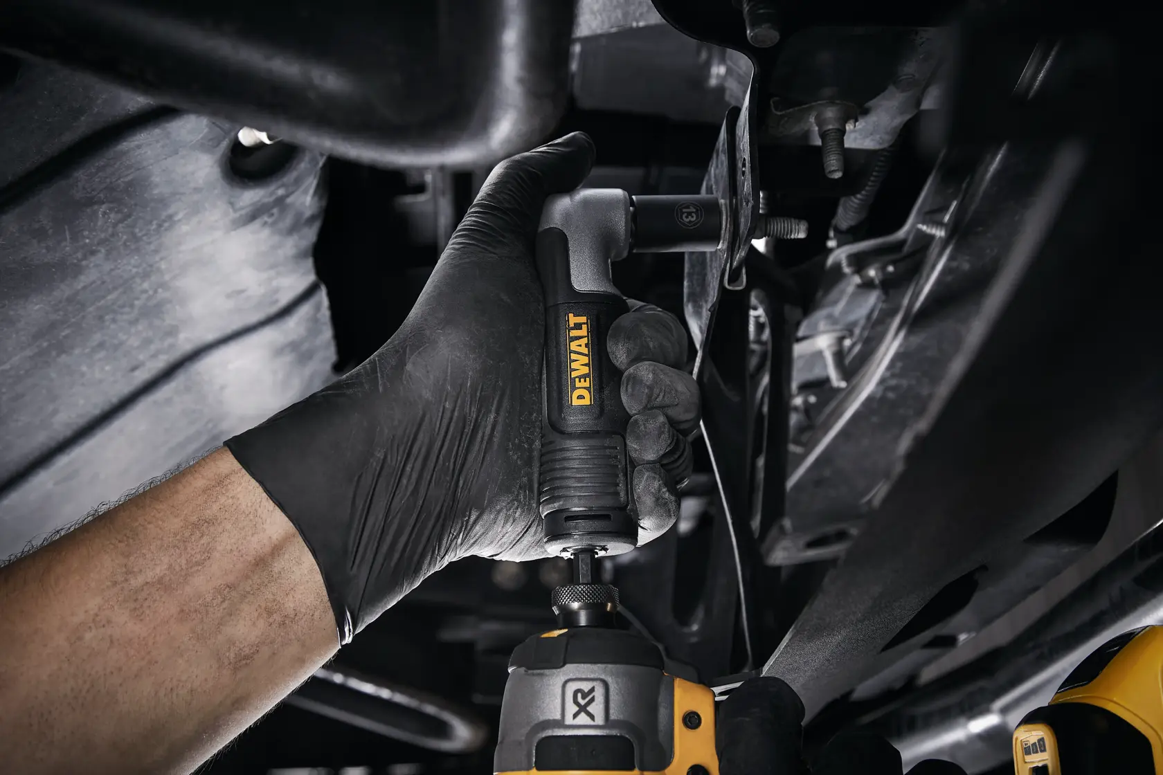 Mão com luva usa adaptador angular DEWALT sob veículo para trabalhos em locais apertados.