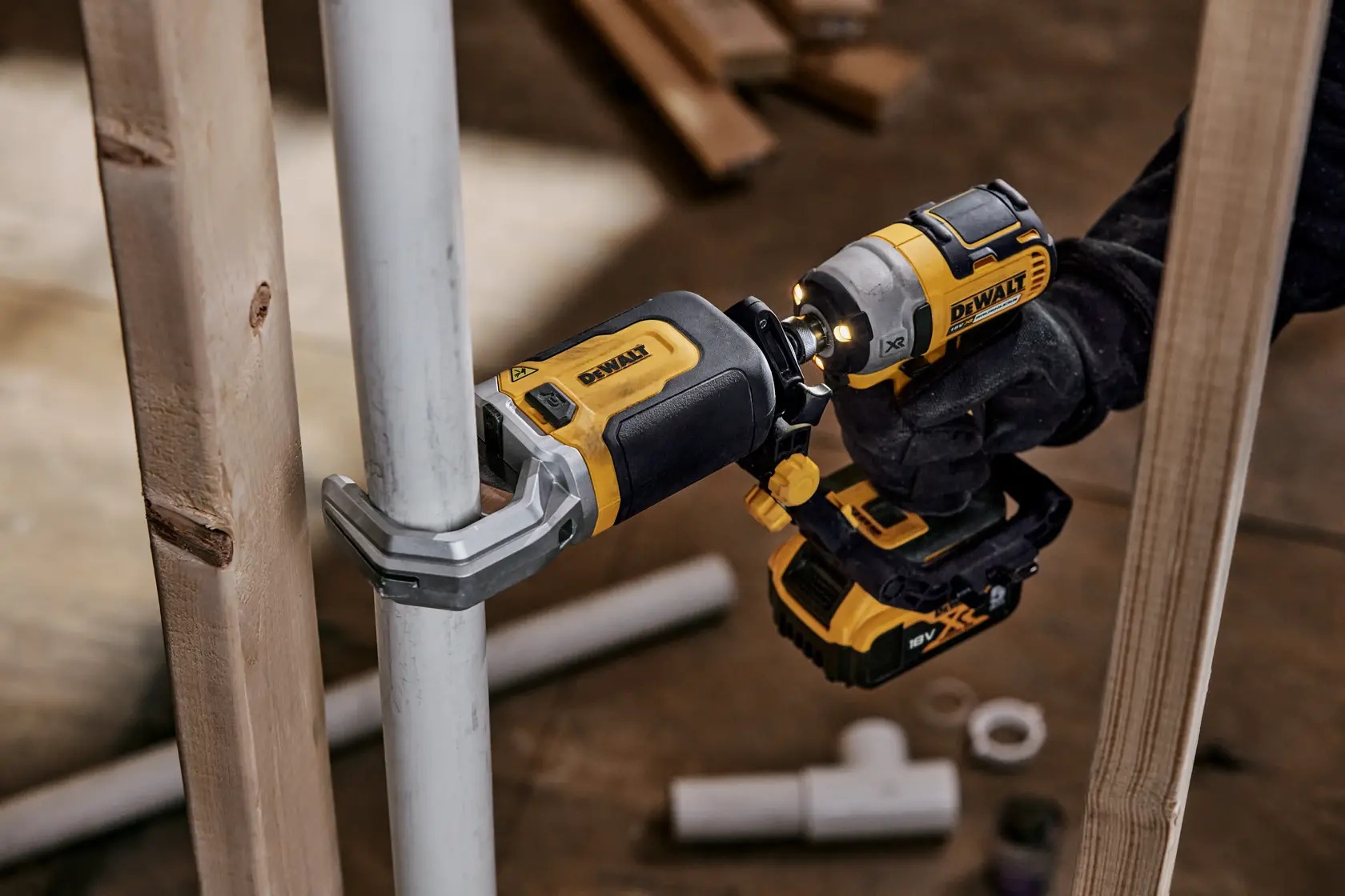 Uma ferramenta elétrica DEWALT DT20560 sendo usada para prender uma braçadeira em um tubo metálico, segurada por uma pessoa com luva. A ferramenta é amarela e preta, com outros tubos e tábuas de madeira ao fundo.