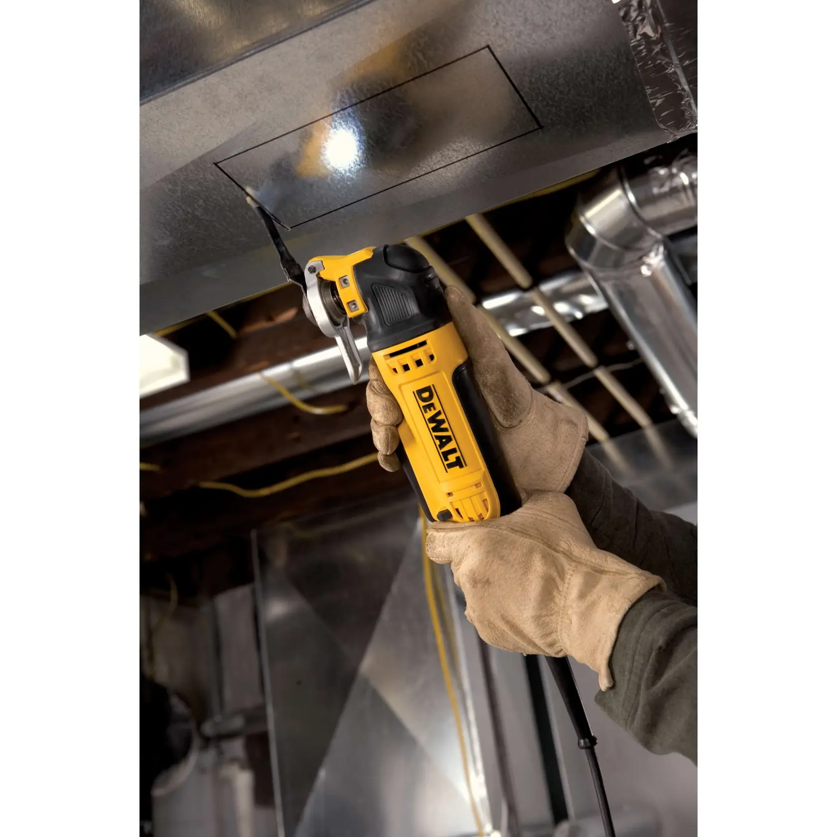 Manos enguantadas usan herramienta oscilante DEWALT para cortar una abertura rectangular en un conducto metálico.