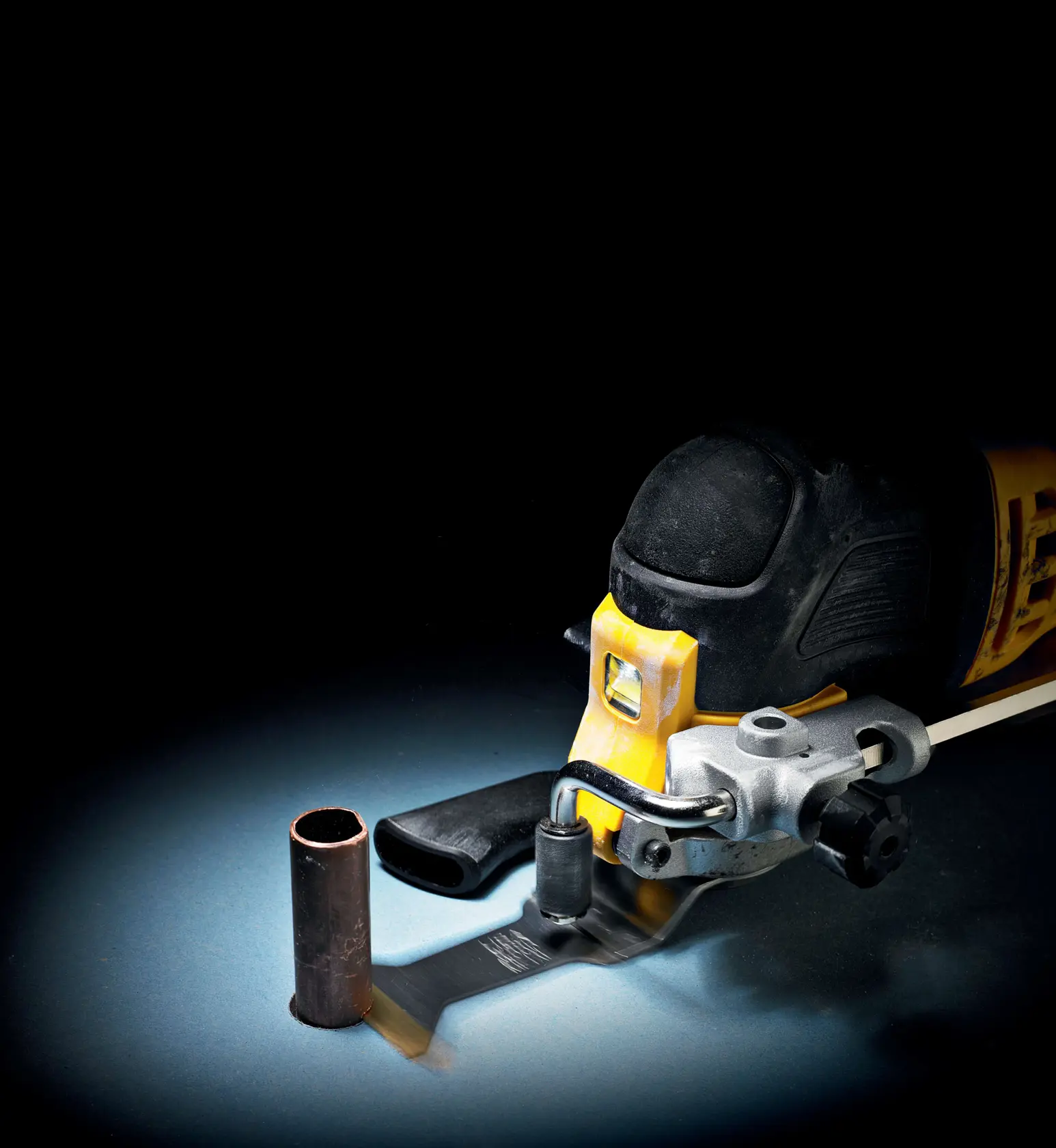 Herramienta oscilante DEWALT cortando un tubo de metal sobre fondo oscuro.