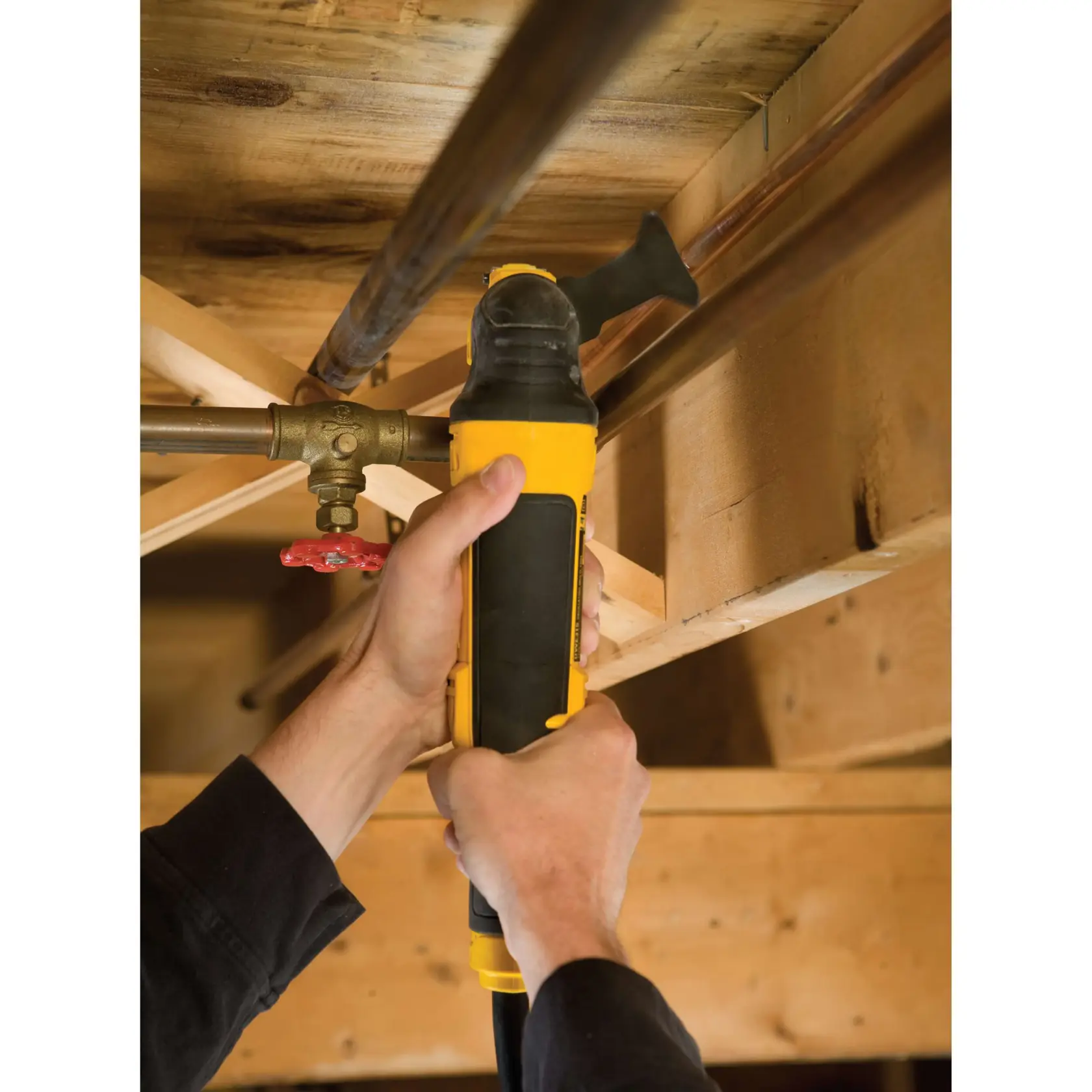 Manos usando herramienta DEWALT para cortar un tubo metálico bajo una estructura de madera.