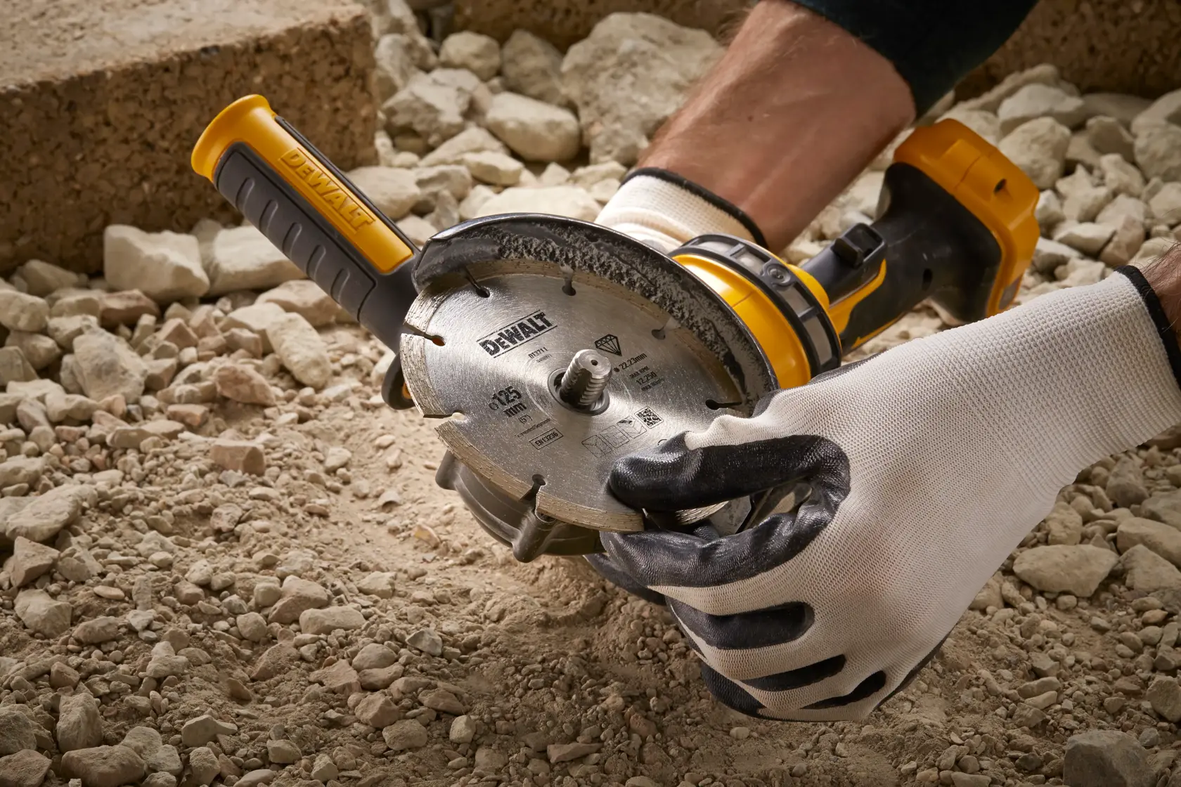 Persona usando herramienta DEWALT DT3559 sobre piedras, con guantes protectores.