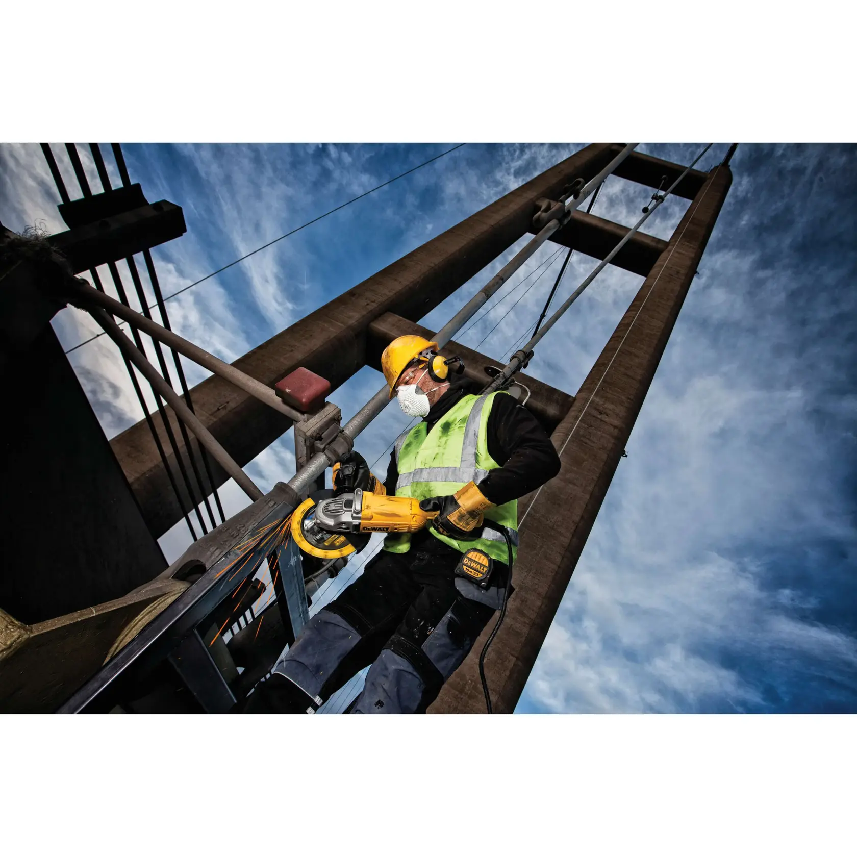 Trabalhador usa ferramenta DEWALT em estrutura metálica ao ar livre, com céu azul ao fundo.