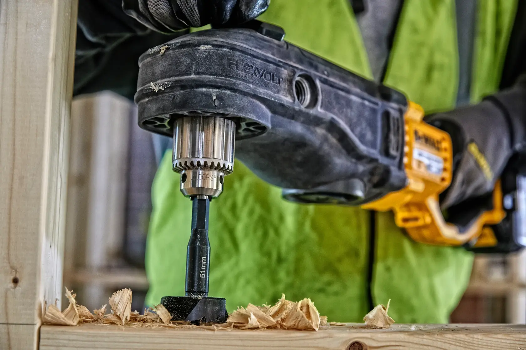 Taladro DEWALT con broca de madera y virutas, persona con guantes y chaleco de seguridad.