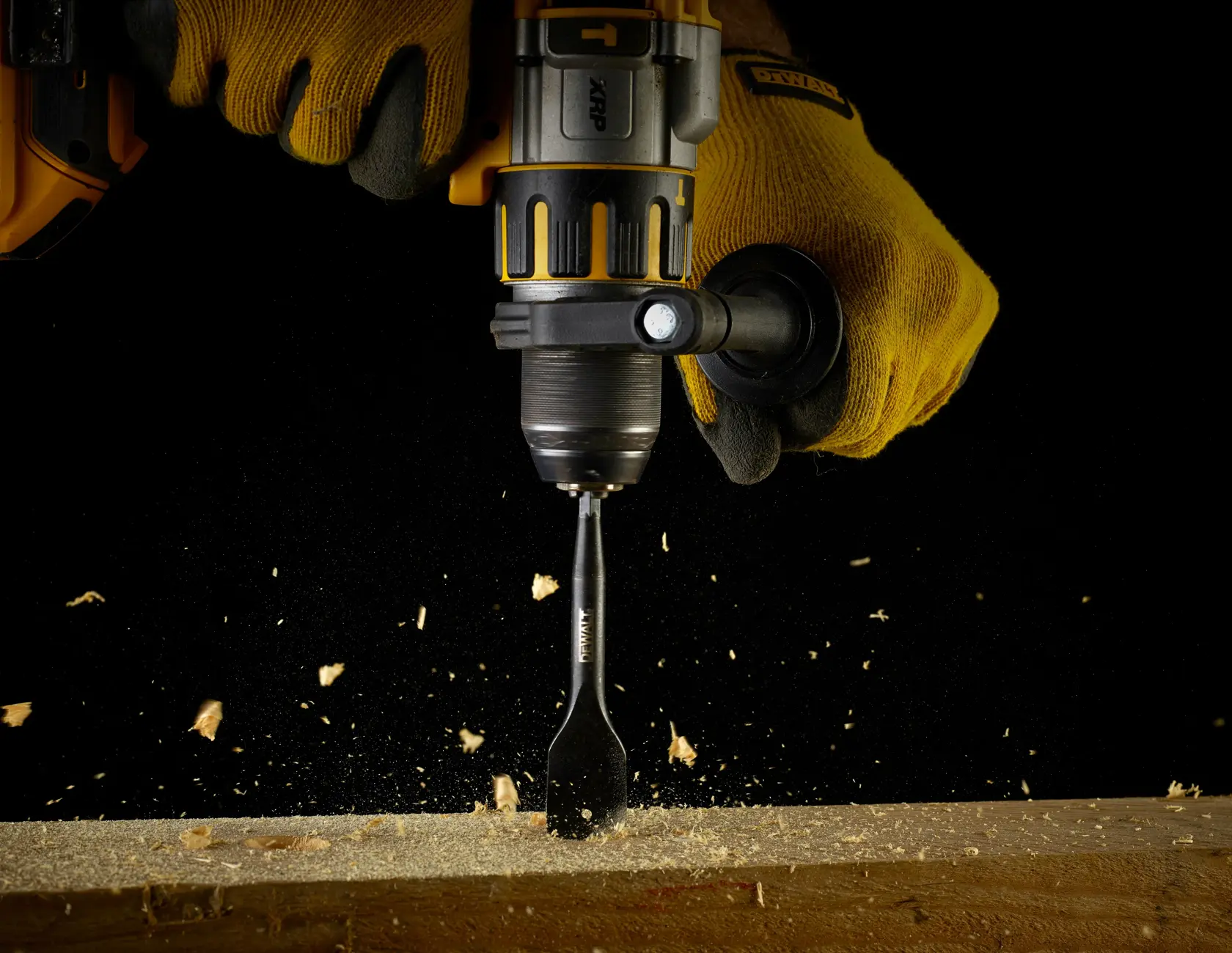 Taladro DEWALT con guantes perforando madera y generando aserrín, fondo negro.