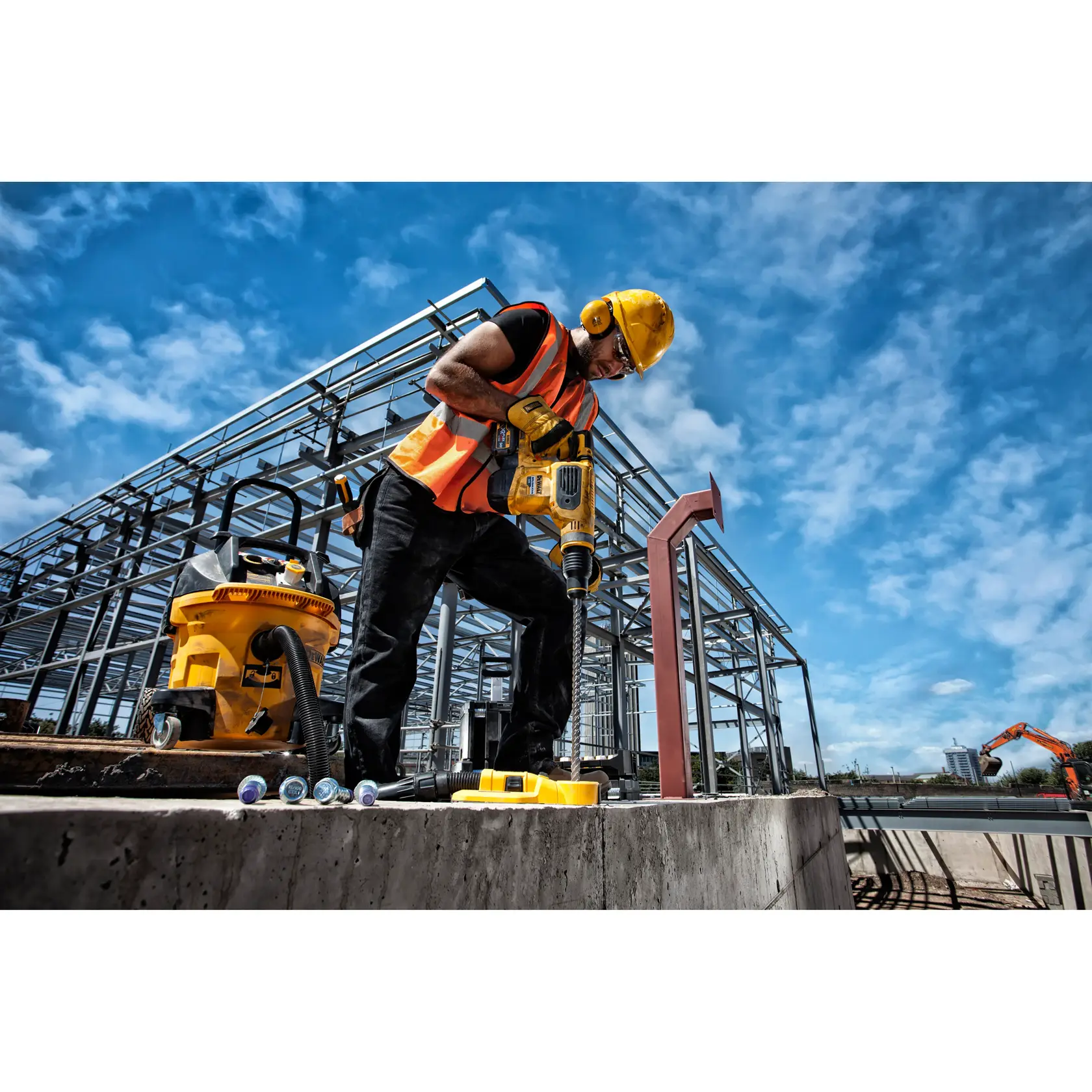 Operário usa furadeira DEWALT em obra com estrutura de aço e equipamentos sob céu azul.