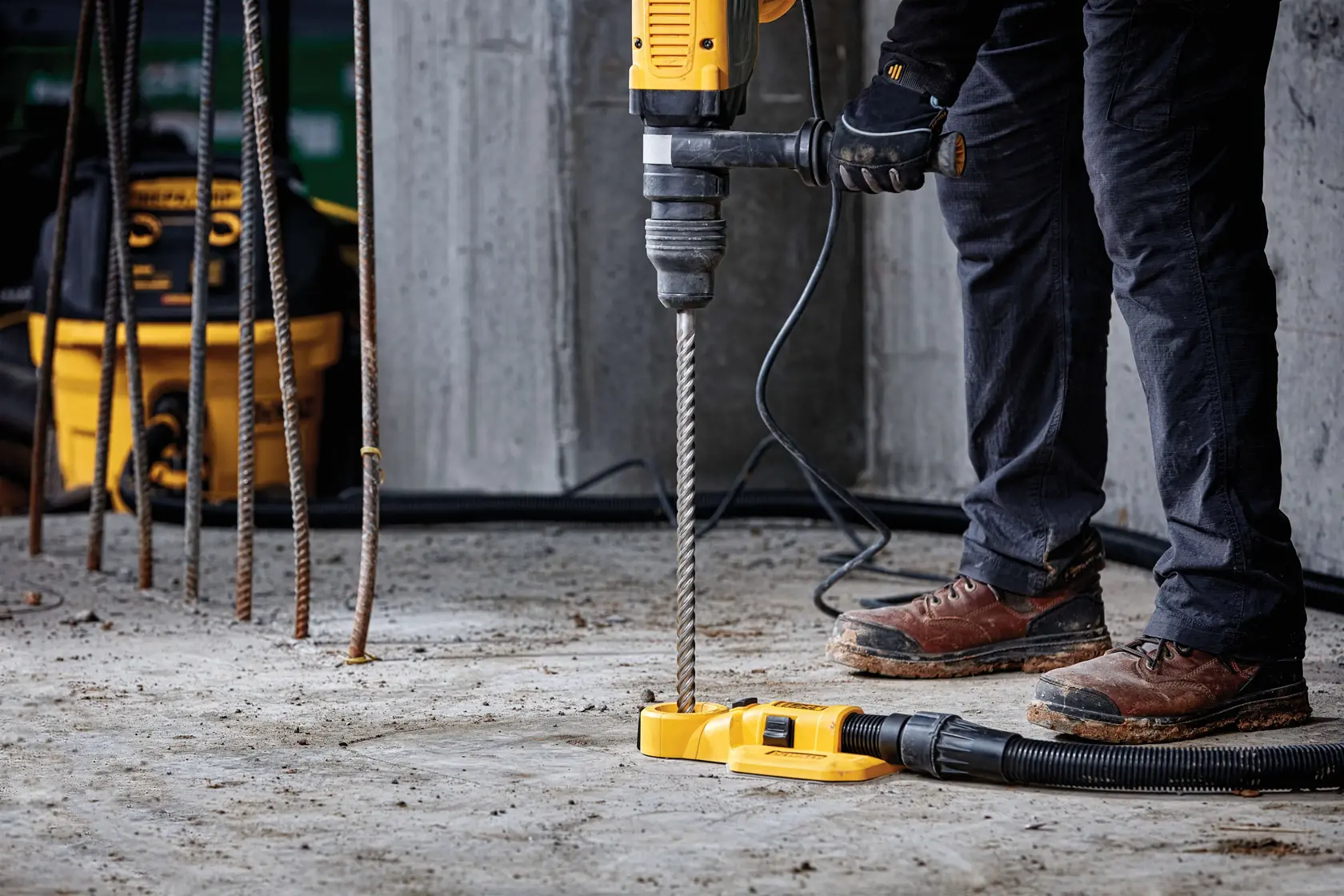 Trabalhador usa furadeira DEWALT com extrator de pó em piso de concreto na obra.