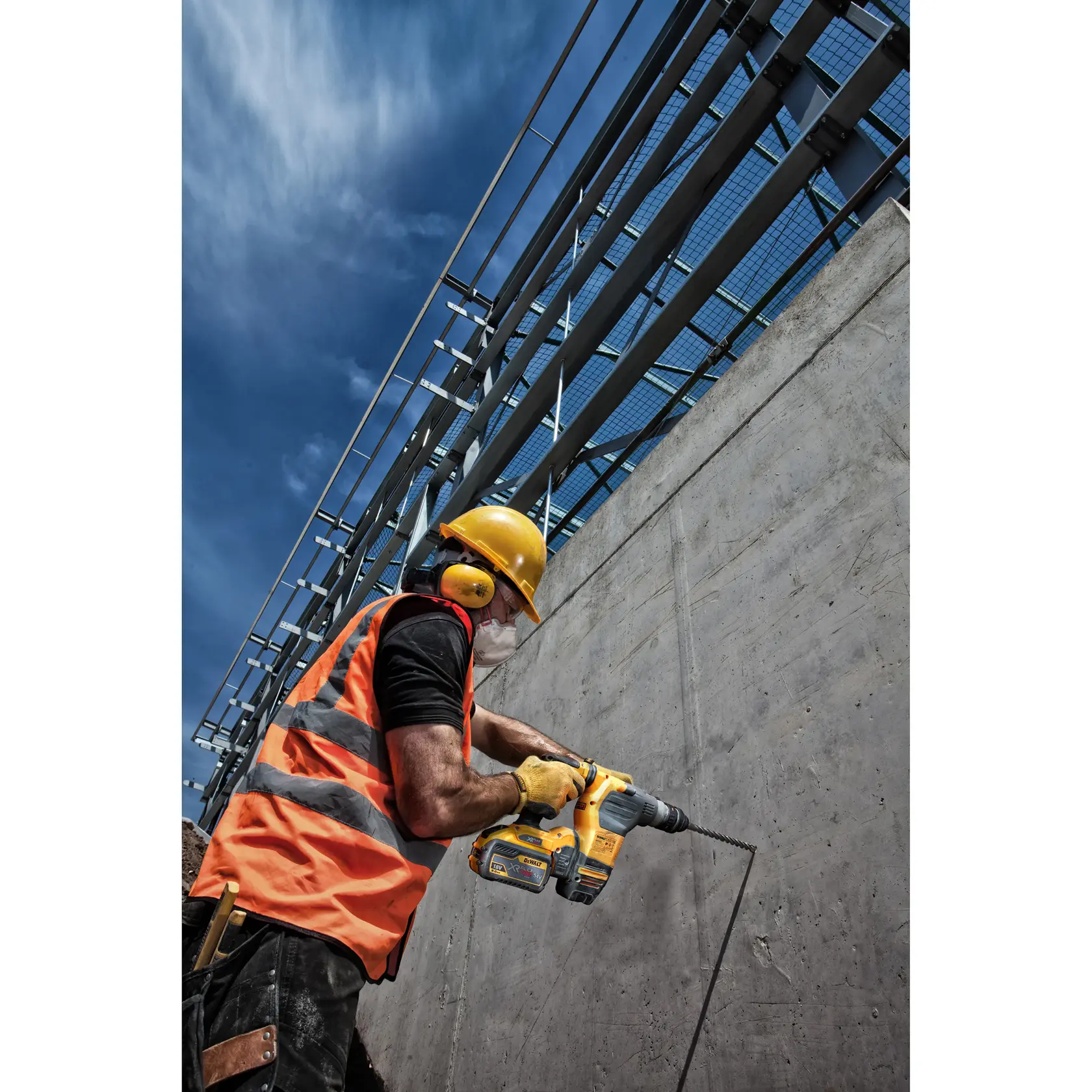 Trabajador con equipo de seguridad usa un taladro DEWALT en una pared de concreto al aire libre.