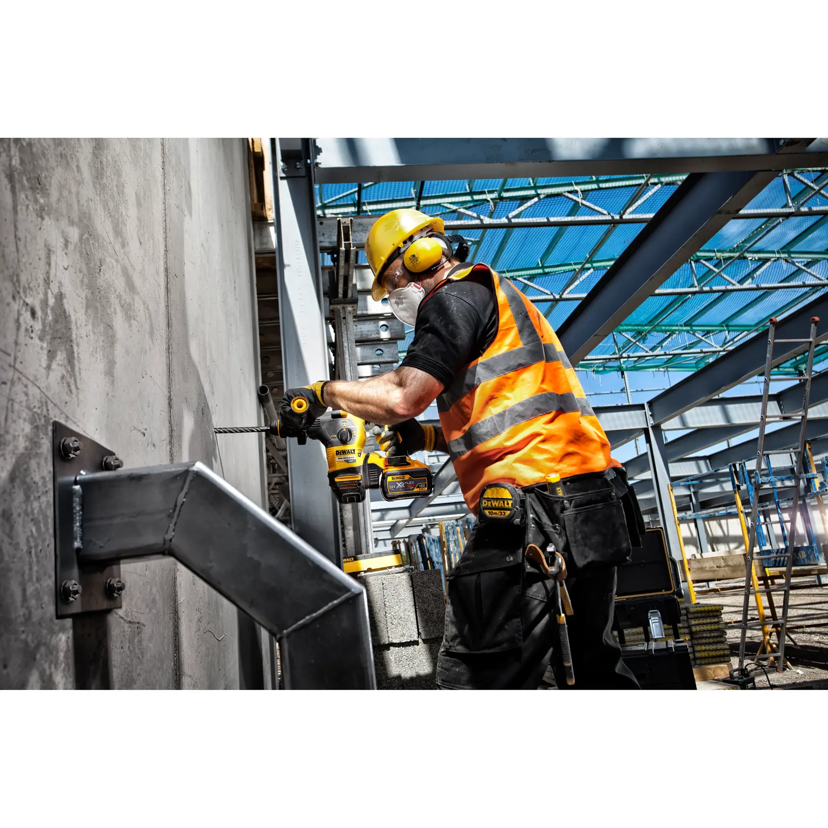 Trabajador usa taladro DEWALT en pared de concreto en obra, con chaleco naranja y equipo de seguridad.
