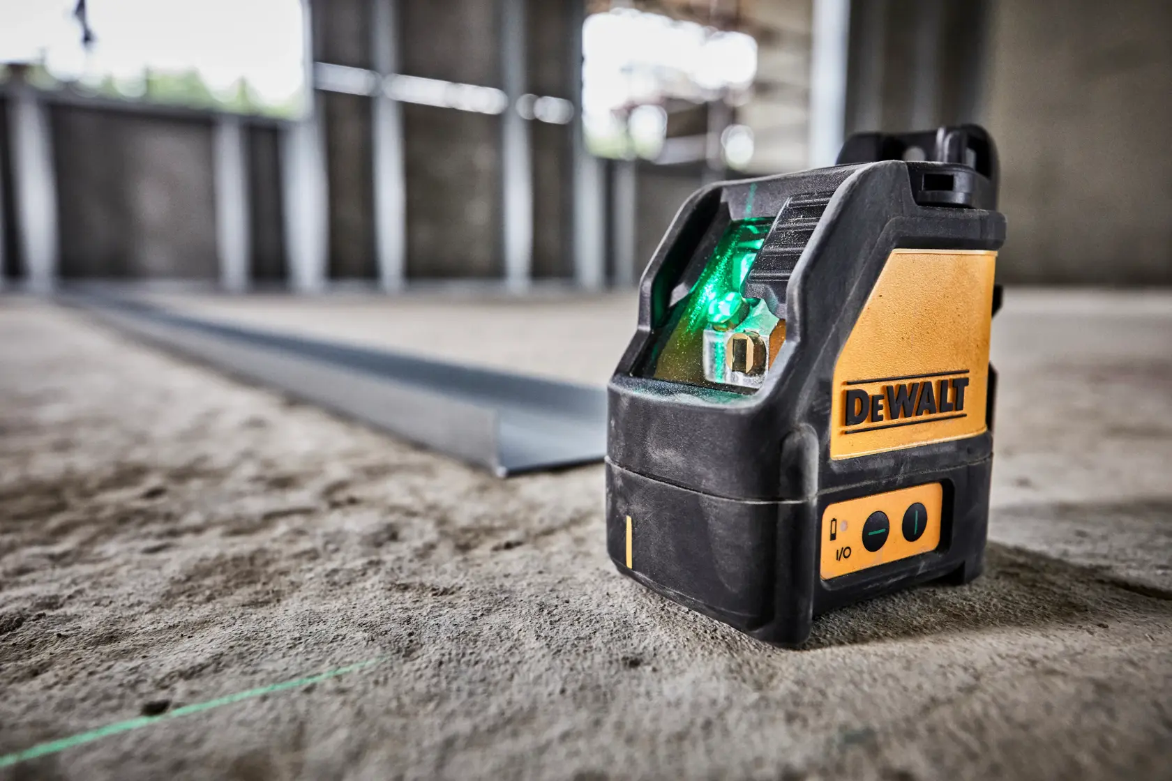 Um nível a laser de linha cruzada verde DEWALT DW088CG colocado em um piso de concreto bruto em um canteiro de obras, projetando uma linha de laser verde para alinhamento preciso.