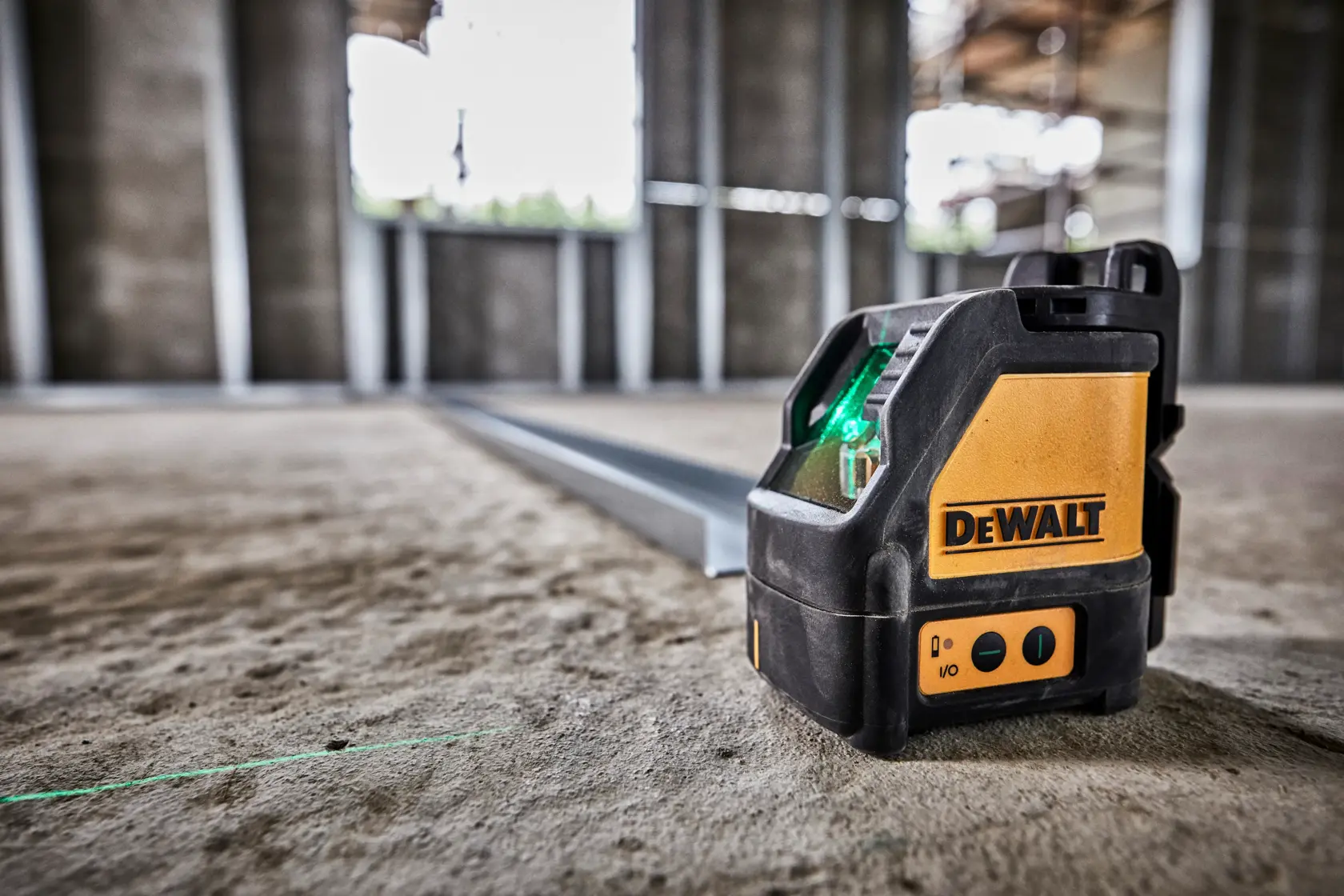 Um nível a laser de linha verde DEWALT colocado sobre um piso de concreto em uma obra não finalizada, projetando uma linha de laser verde visível para alinhamento.