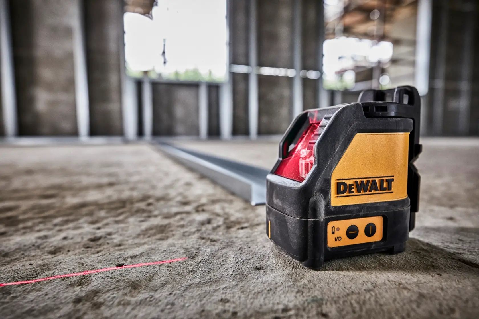 Um nível a laser de linha cruzada auto-nivelante DEWALT DW088K colocado no chão de um canteiro de obras, projetando uma linha de laser vermelha visível para tarefas de alinhamento.