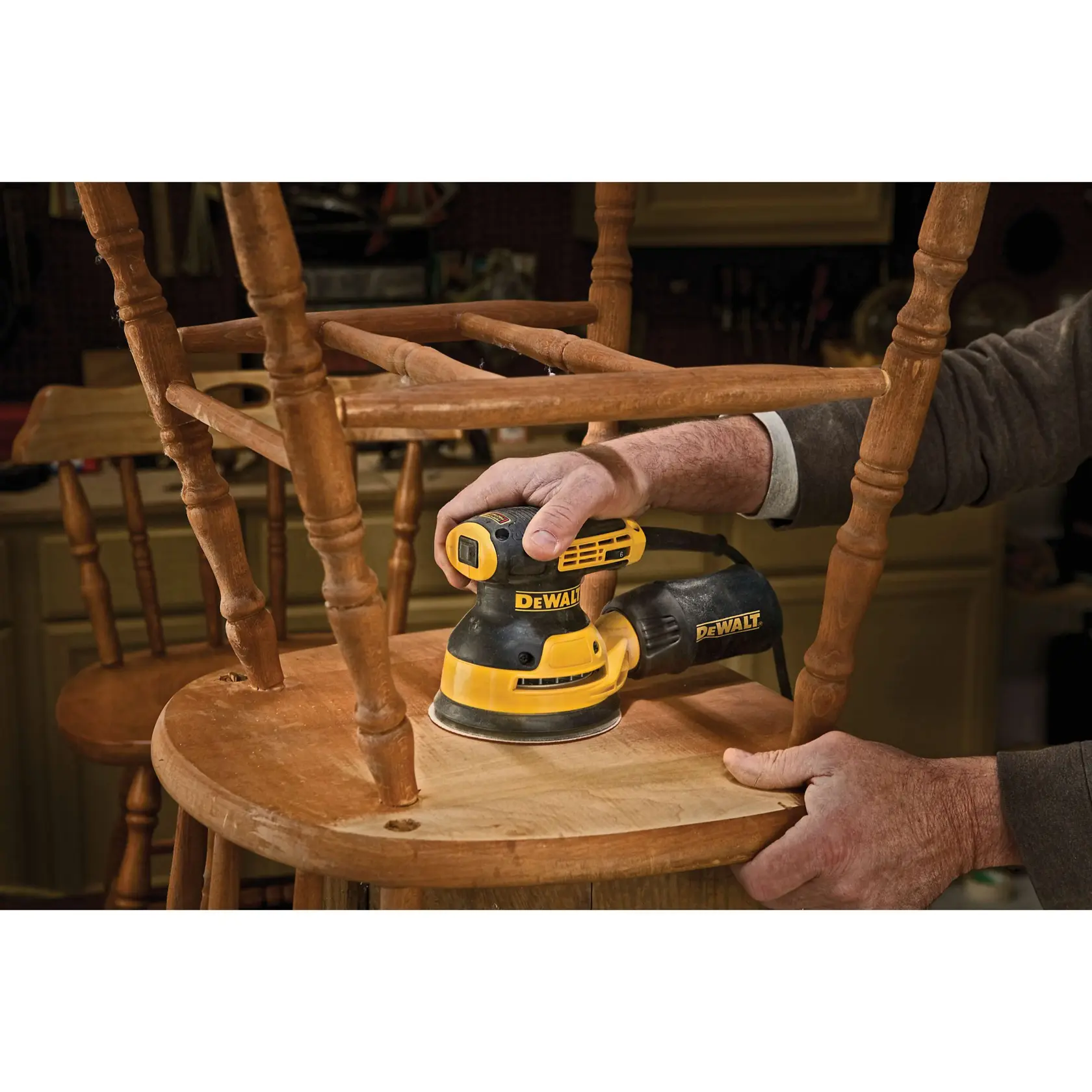Uma pessoa usa uma lixadeira orbital aleatória DEWALT DWE6423 para lixar uma porta de madeira em uma oficina de marcenaria. Algumas peças de ferragem de metal estão posicionadas na mesa próxima, e a pessoa está usando uma máscara de proteção.