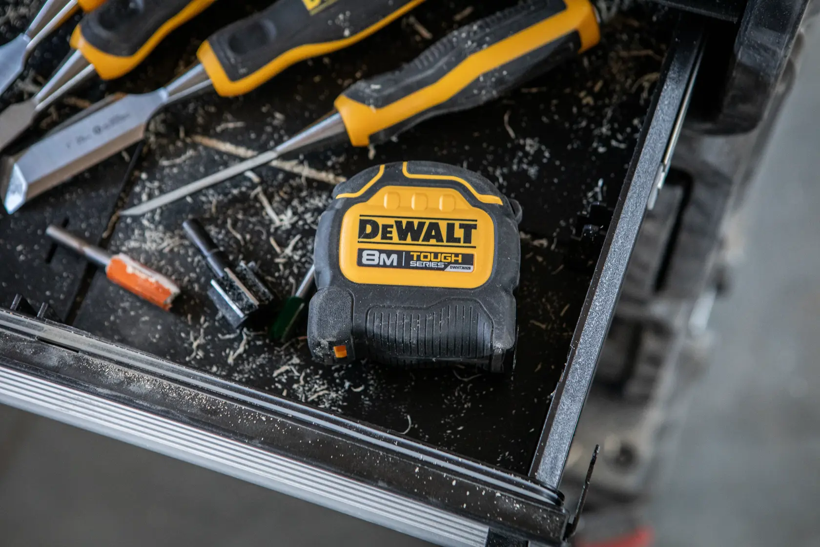 Trena DEWALT 8m na bancada com ferramentas e parafusadores, cercada por cavacos de madeira.