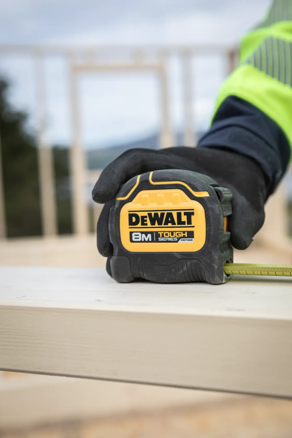 Trena DEWALT 8M Tough Series segurada por mão com luva em tábua de madeira numa obra.