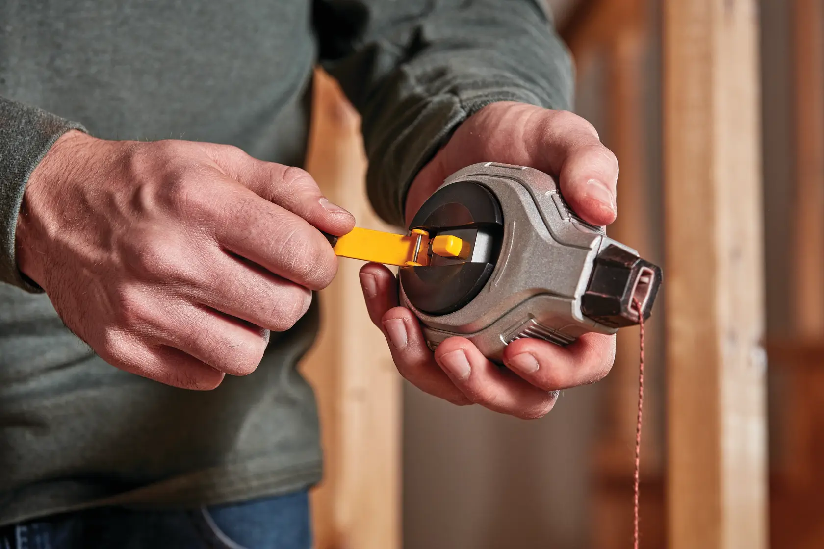 Pessoa segurando e enrolando um marcador de linha DEWALT com alça amarela em ambiente de construção.